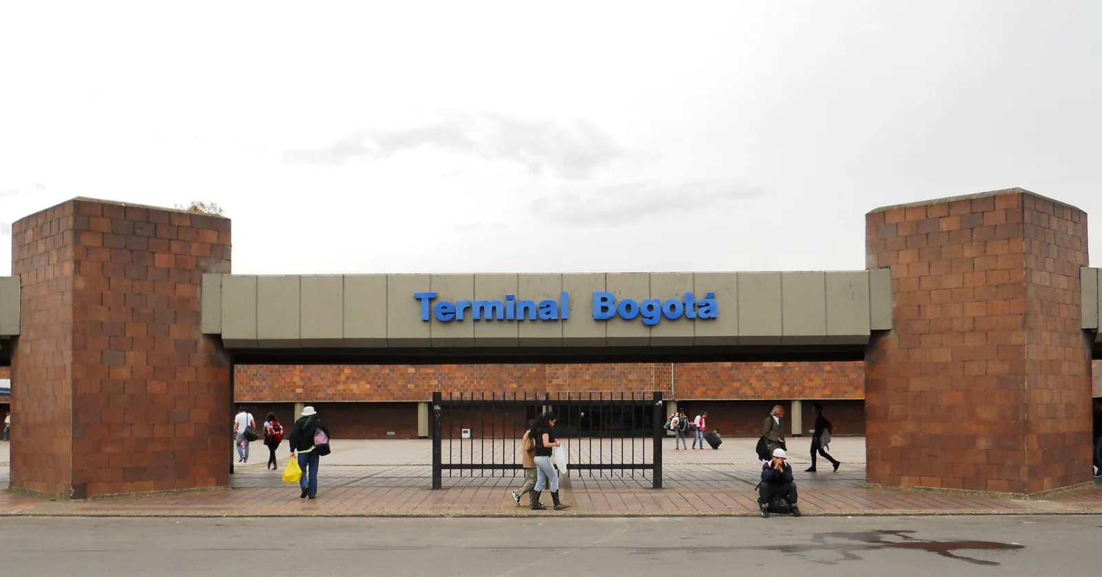 The entrance to Bogotá's Salitre intercity bus terminal, a low canopy between two brick columns with the name across it and travellers walking through with wheeled luggage