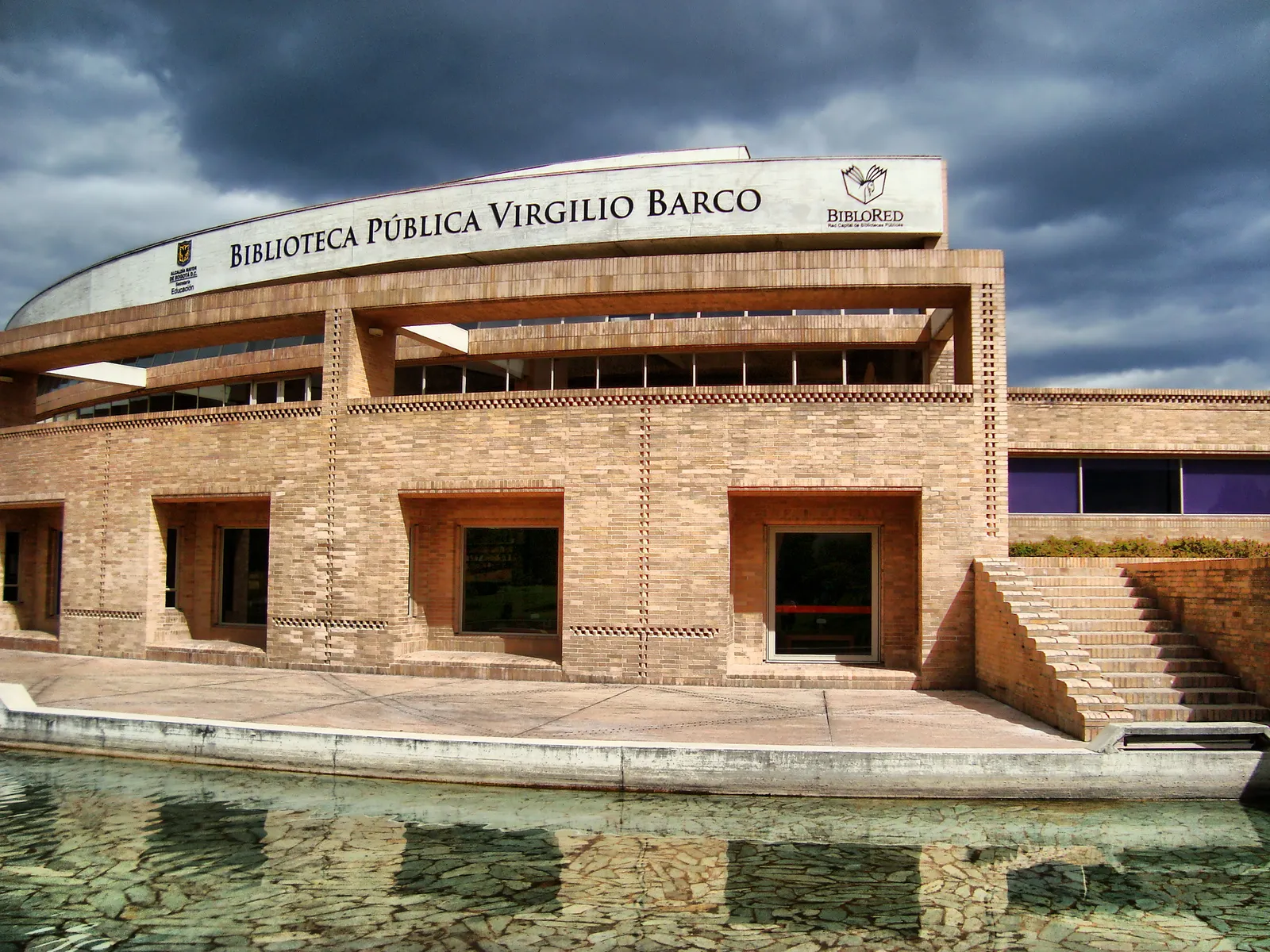 The Virgilio Barco library in Bogotá, a curved brick building with its name on a long canopy above the entrance and a shallow reflecting channel running along the front