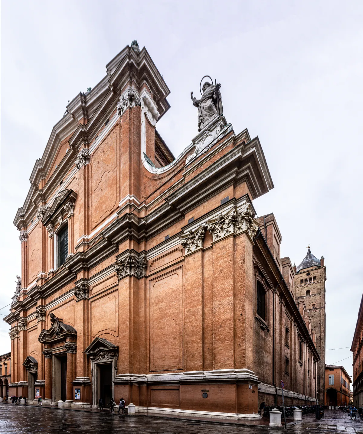 The brick and stone Baroque front of Bologna's Cathedral of San Pietro on Via dell'Indipendenza, a statue on its gable and the tall brick bell tower rising behind on the right