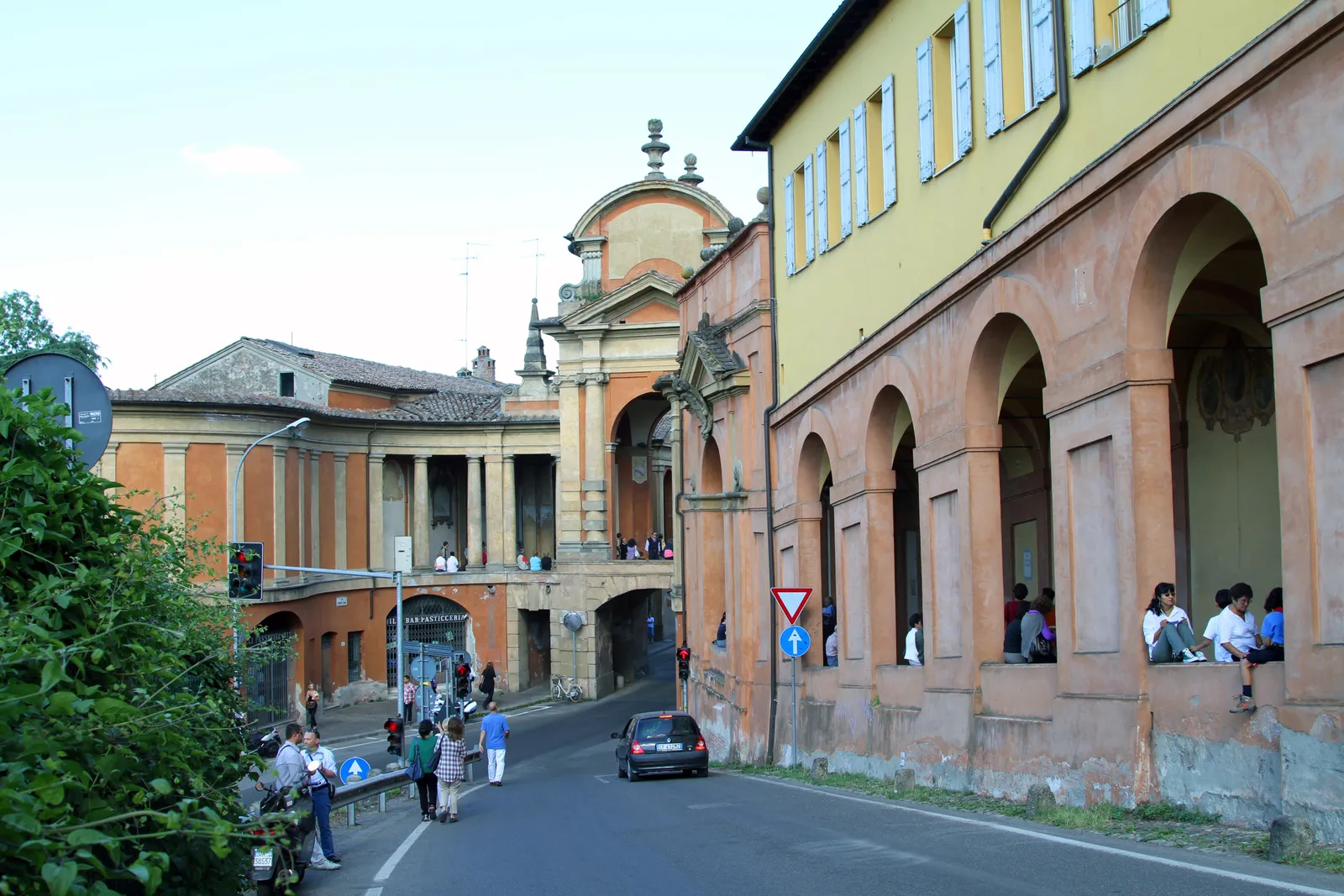 The Arco del Meloncello in Bologna, a curved Baroque arch carrying the San Luca portico over Via Saragozza, with the arcade continuing alongside the road