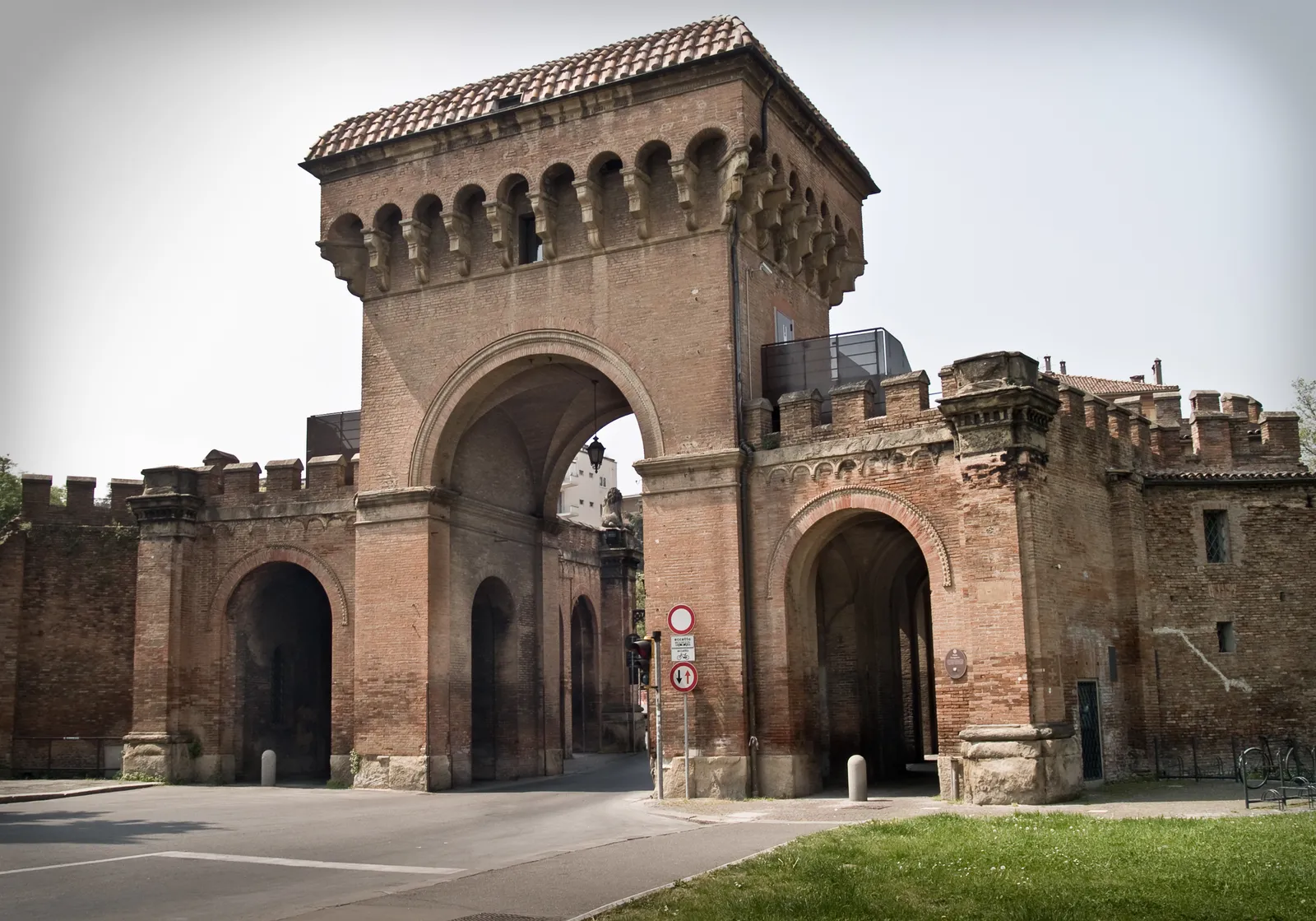 Porta Saragozza in Bologna, a brick city gate with a crenellated central tower over a tall archway, joined by walls and smaller arches to the towers either side