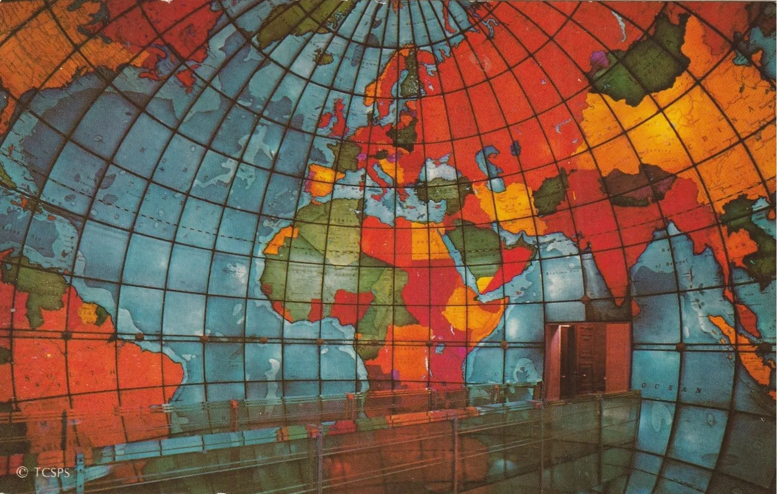 The inside of the Mapparium in Boston, a hollow stained-glass globe of continents in red, orange and blue lit from behind, with a walkway running through the middle of it