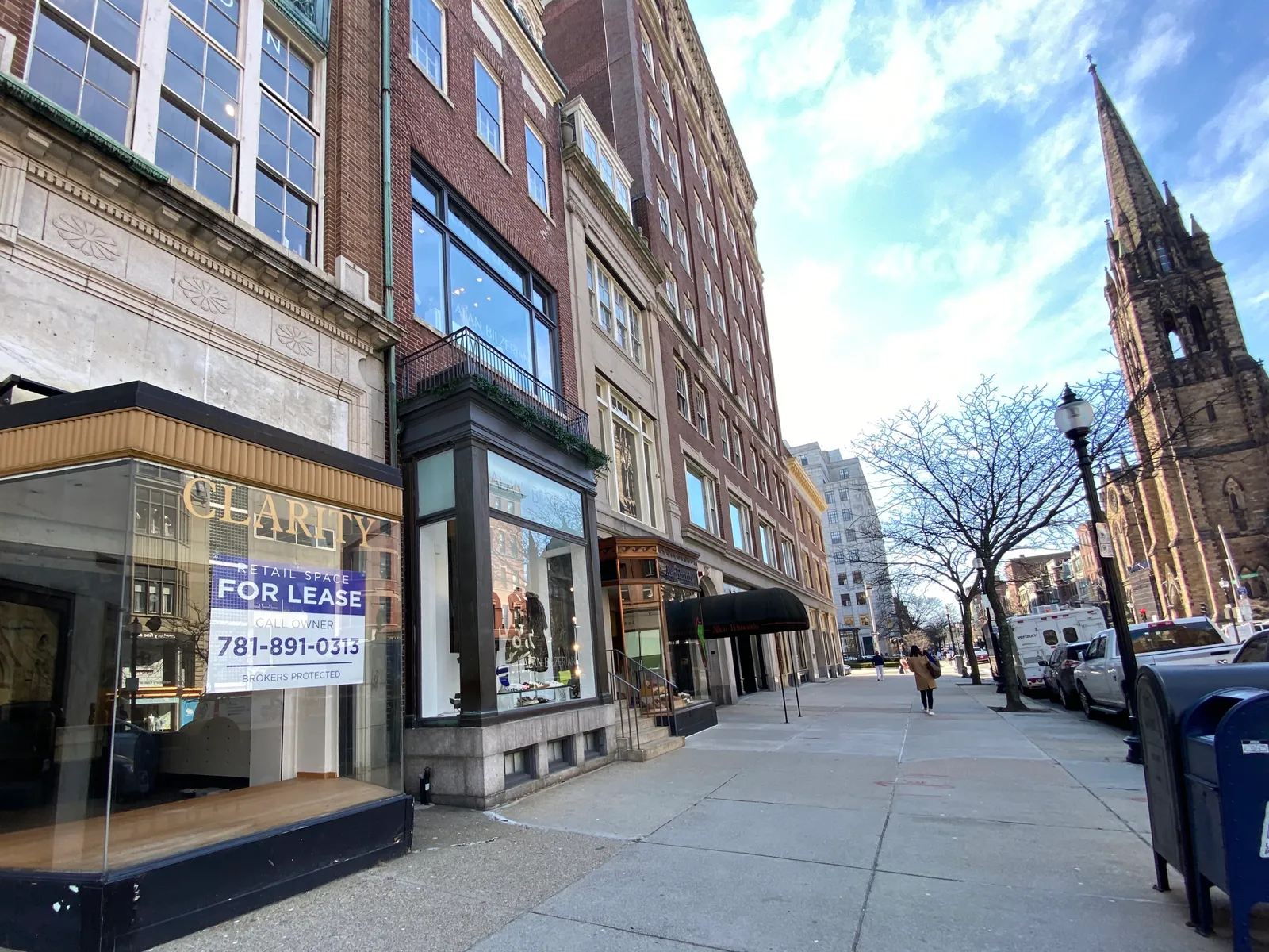 A block of Newbury Street in Boston, shopfronts fitted into the basement and parlour floors of brownstone houses, with a church spire further down the street