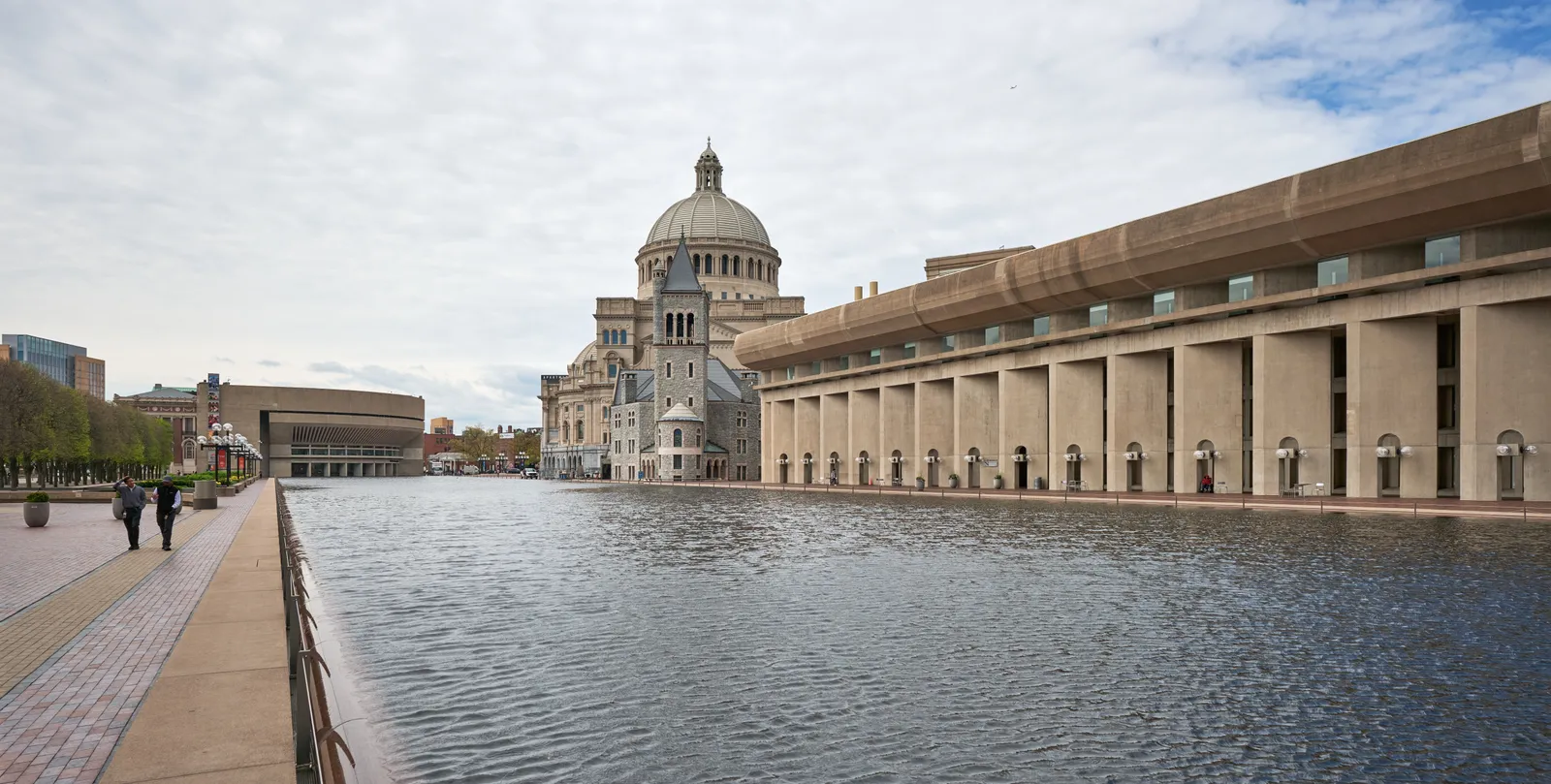 The long reflecting pool on Christian Science Plaza in Boston, water level with its granite edge, the domed Mother Church at the far end and a colonnade running down the right-hand side