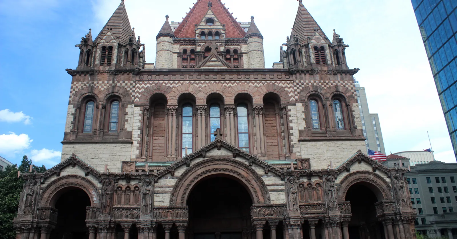 The west front of Trinity Church on Copley Square in Boston, three deep arched portals in banded granite and brownstone under a pair of pinnacled towers