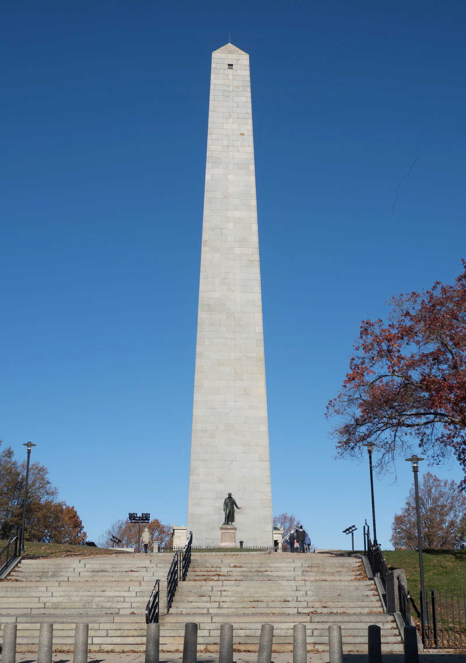The Bunker Hill Monument in Charlestown, Boston, a plain granite obelisk rising from a lawn behind a broad flight of steps, with a bronze statue standing at its base