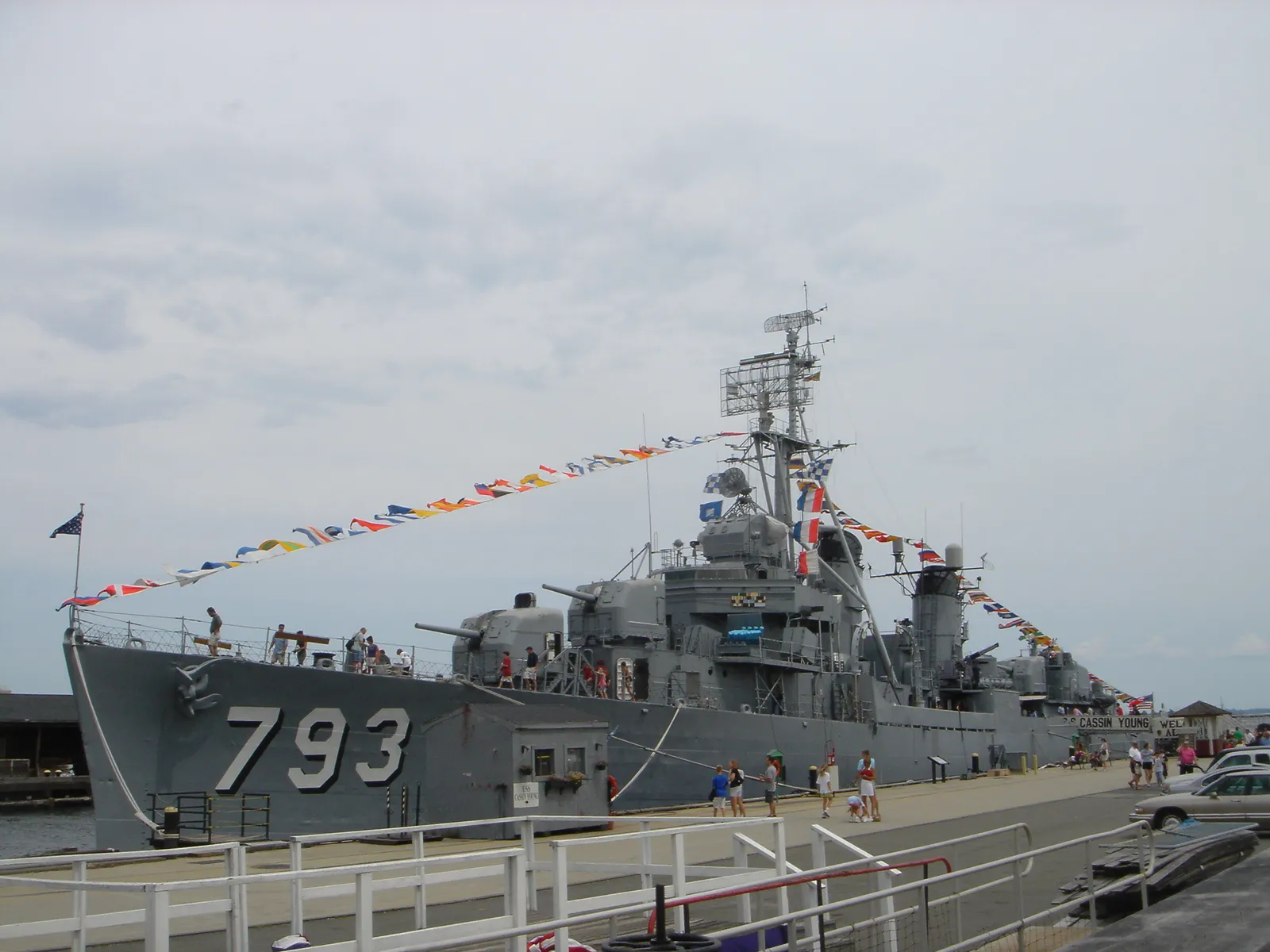 The destroyer USS Cassin Young moored at a pier in Boston, hull number 793 painted on her grey bow and signal flags strung from bow to masthead