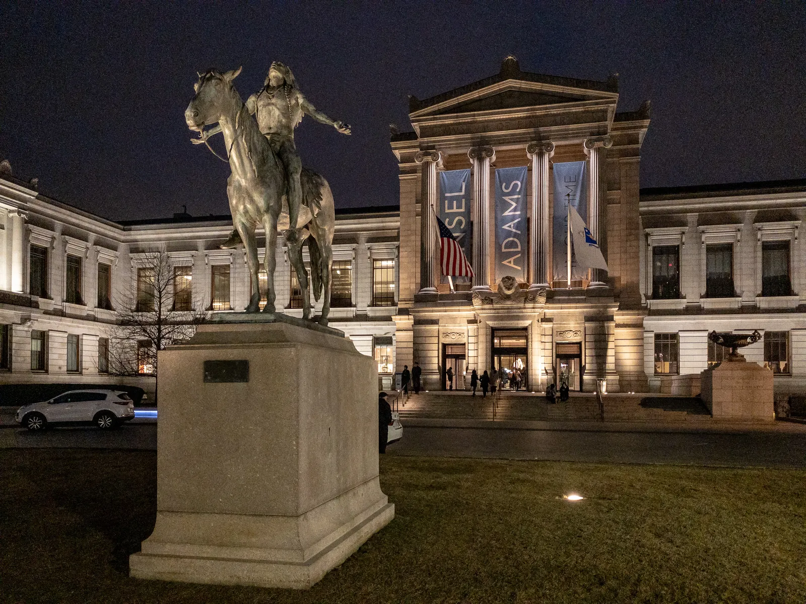 The Huntington Avenue front of the Museum of Fine Arts in Boston lit at night, its columned portico behind a bronze equestrian statue on a granite plinth