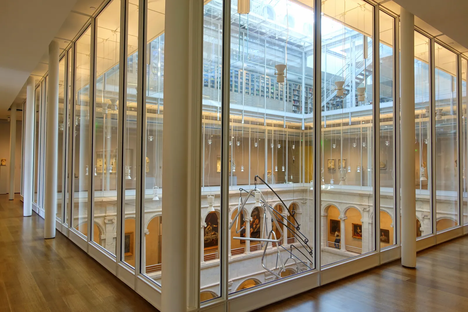 The glazed inner wall of a gallery at the Harvard Art Museums looking into the arcaded stone courtyard, with daylight coming down from the glass roof above