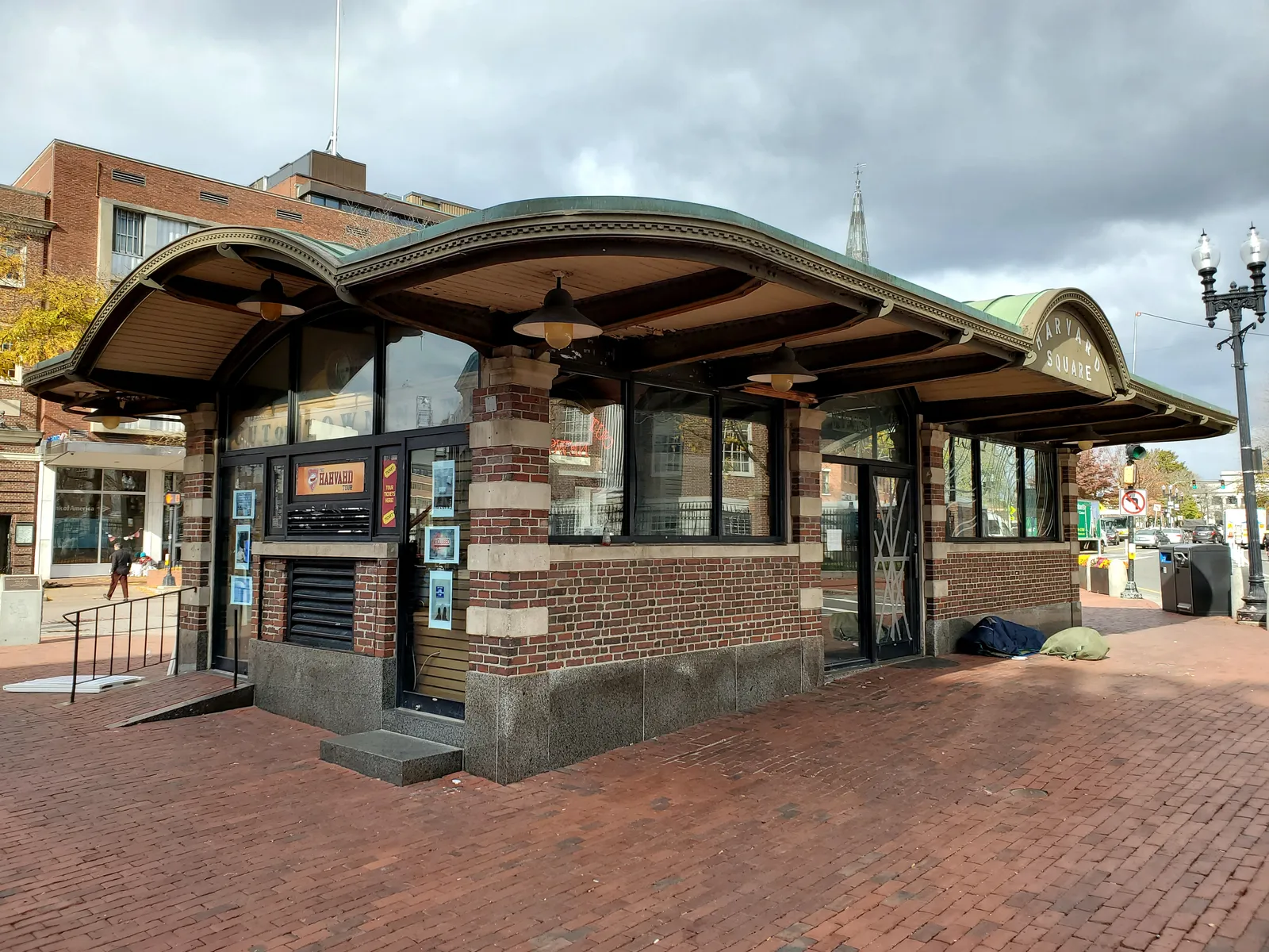 The brick and copper kiosk in Harvard Square, Cambridge, its curved verandah roof carried on brick piers over a brick-paved plaza