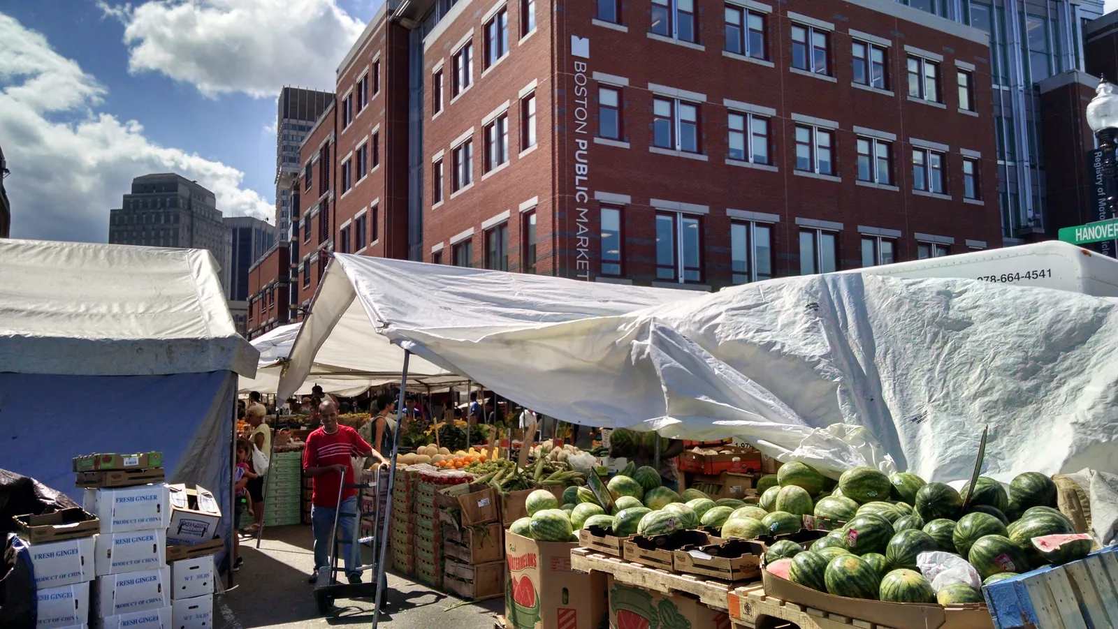 Haymarket in Boston, canvas-topped stands stacked with watermelons and boxed produce along the kerb, with the brick Boston Public Market building behind them