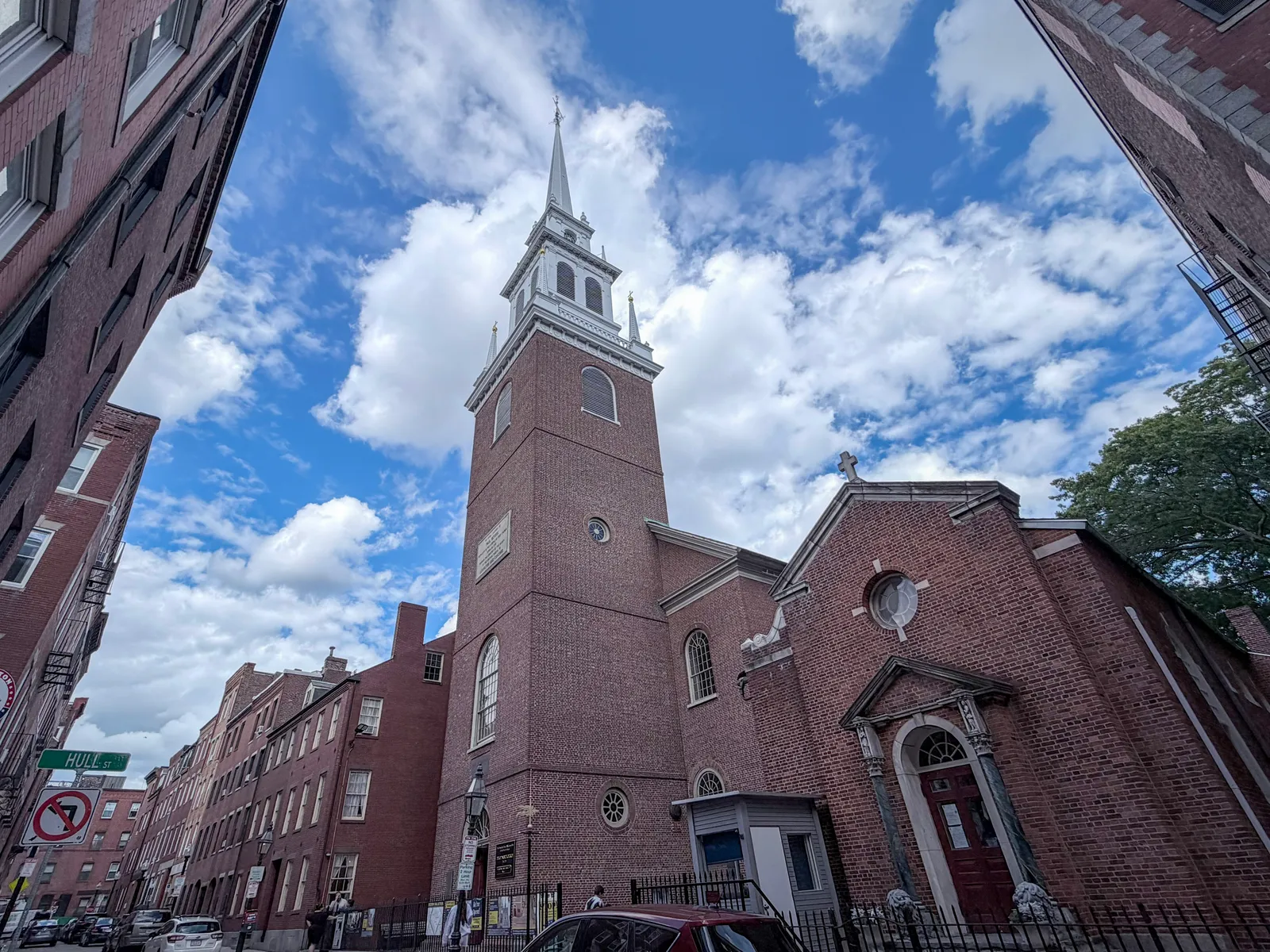The brick body and white timber spire of Old North Church on Salem Street in Boston, seen from the pavement between the brick houses either side of it