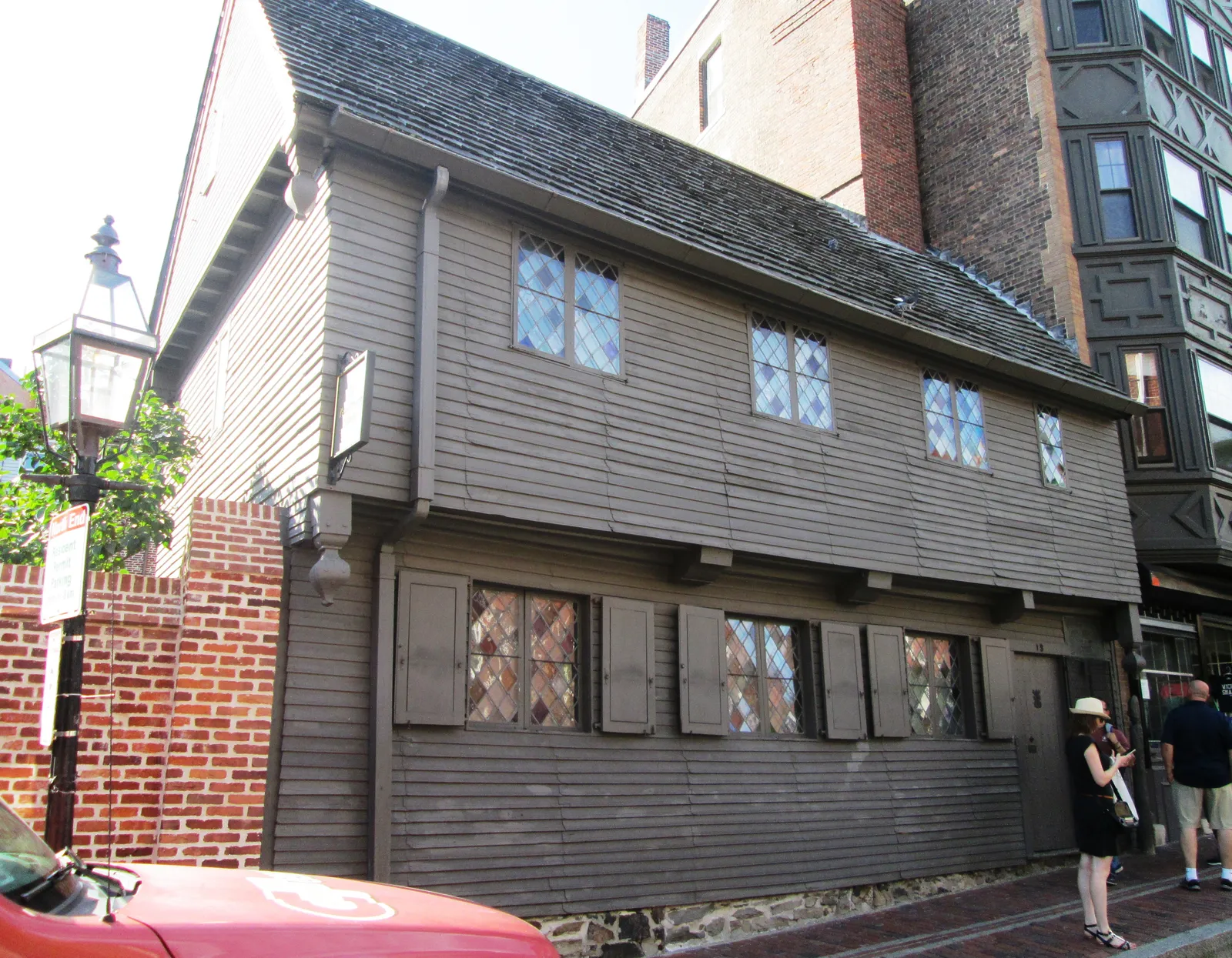 The Paul Revere House in Boston, a two-storey grey clapboard house with an overhanging upper floor, diamond-paned leaded windows and a steep shingled roof, hemmed in by later brick buildings