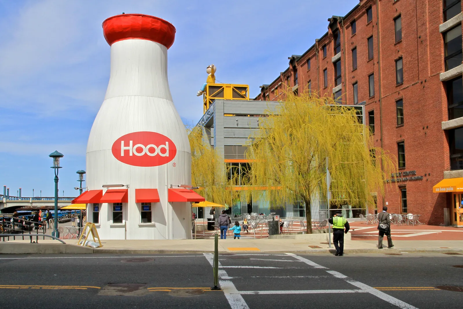 The Hood milk bottle in Boston, a 40-foot white wooden bottle with a red cap and a red Hood oval on its side, standing on the plaza beside a red-brick warehouse block