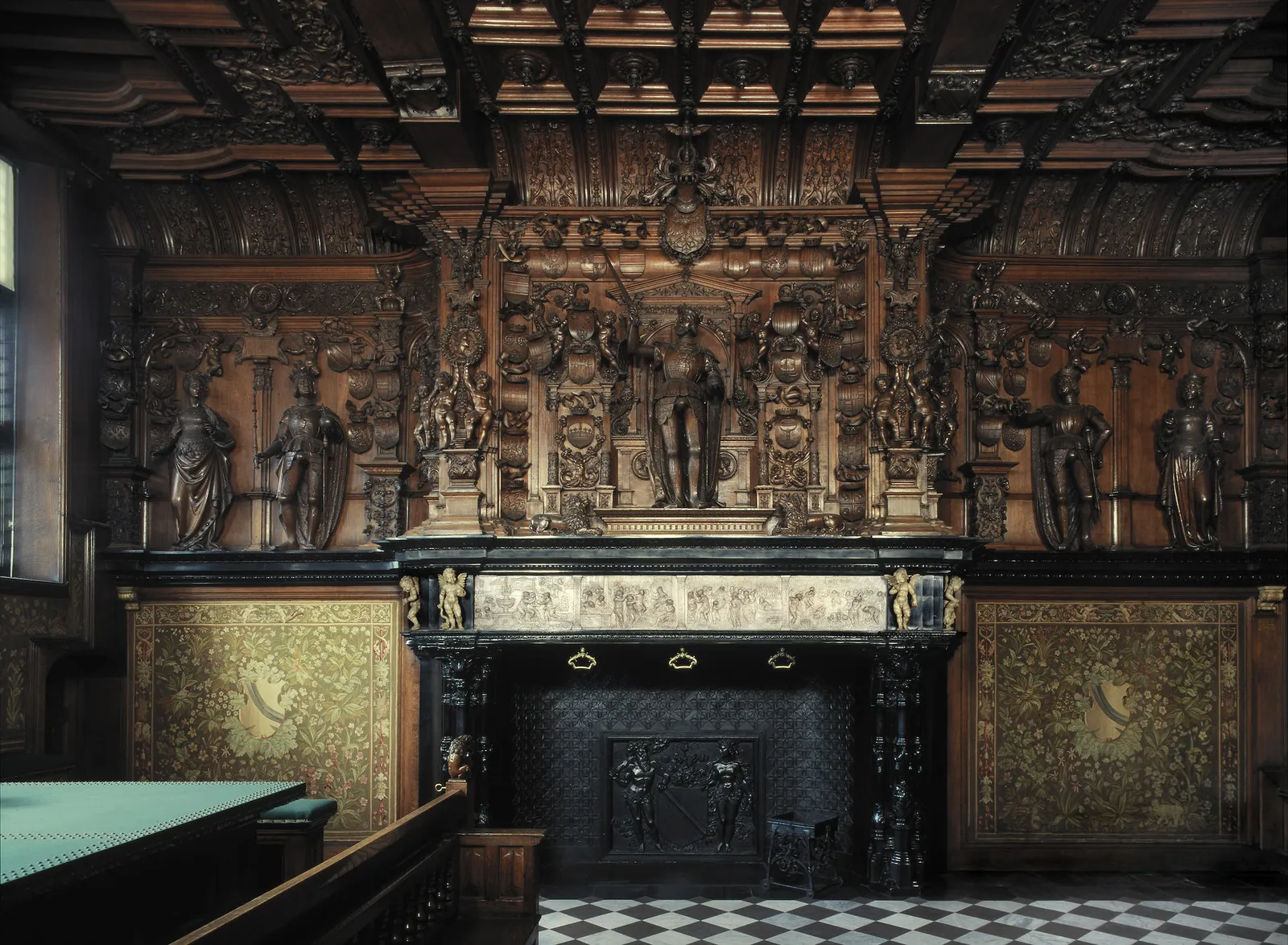 The carved oak mantelpiece in the Liberty of Bruges, five standing royal figures in a dark carved surround above a black marble fireplace with a pale alabaster frieze across it
