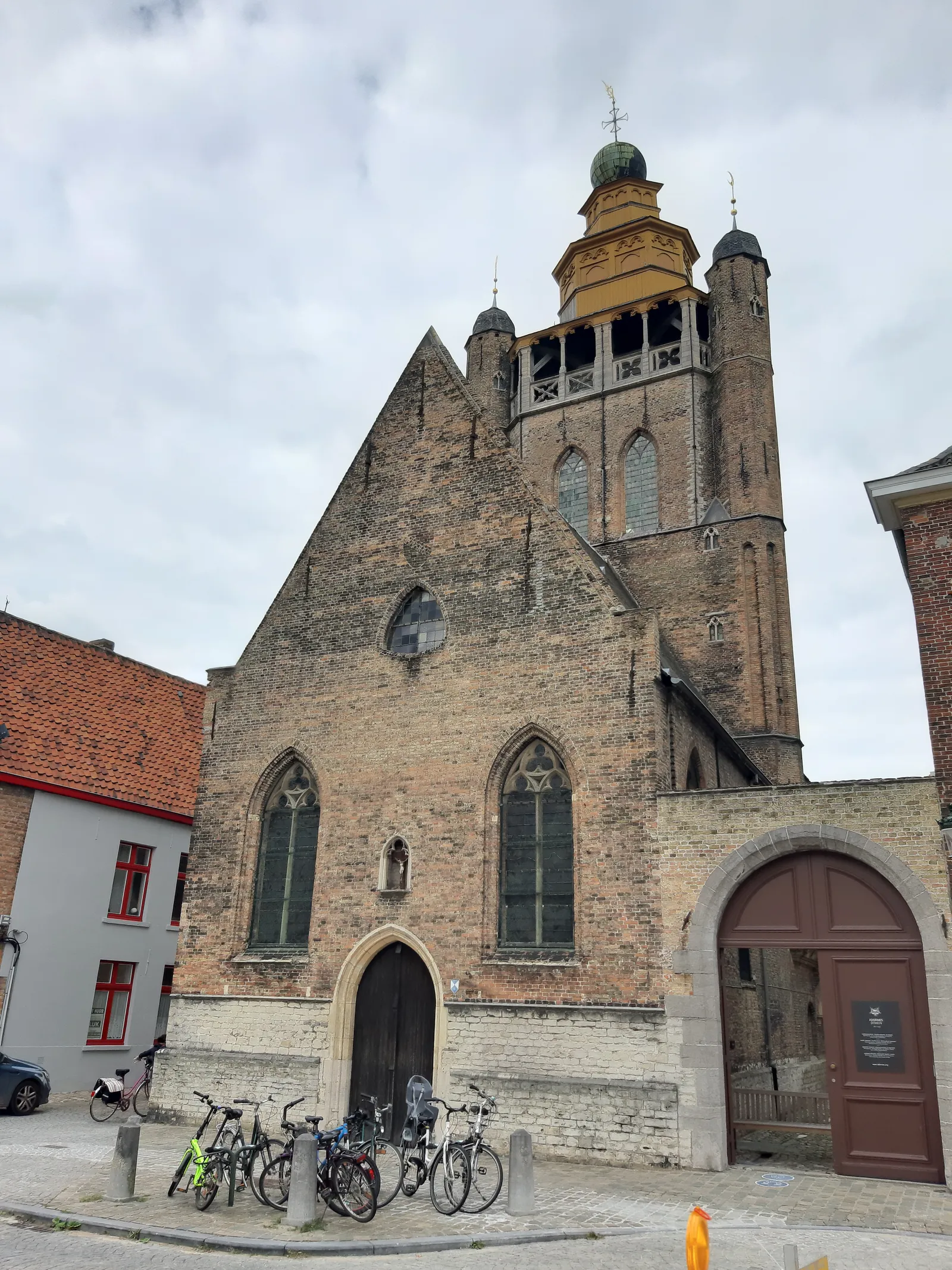 The Jerusalem Chapel in Bruges, a brick church with a stepped gable and an octagonal wooden lantern tower topped by a gilded dome and a cross, bicycles parked against the wall below