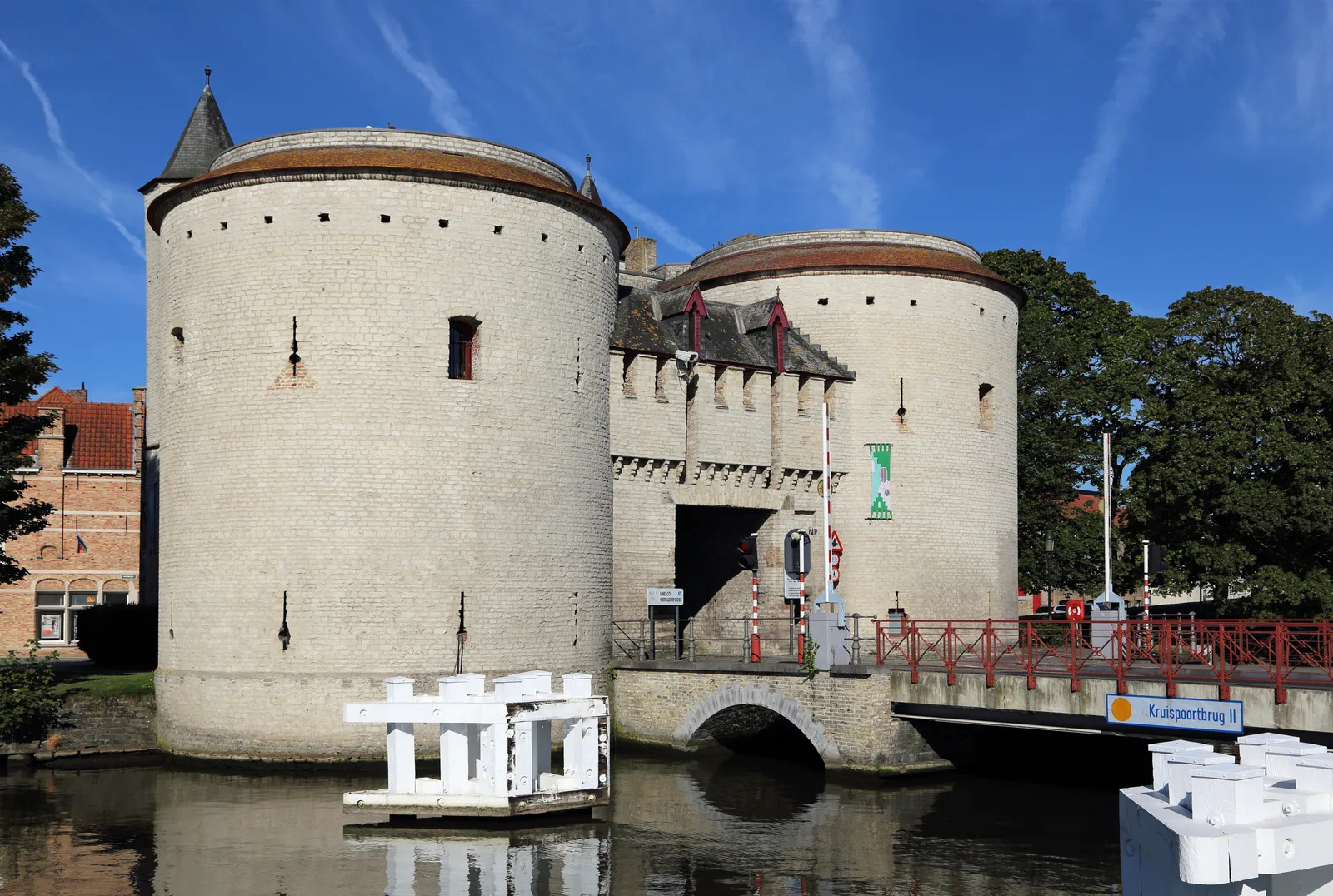 The Kruispoort in Bruges, two tall round stone towers linked by a gatehouse over the road, standing at the end of a bridge across the canal