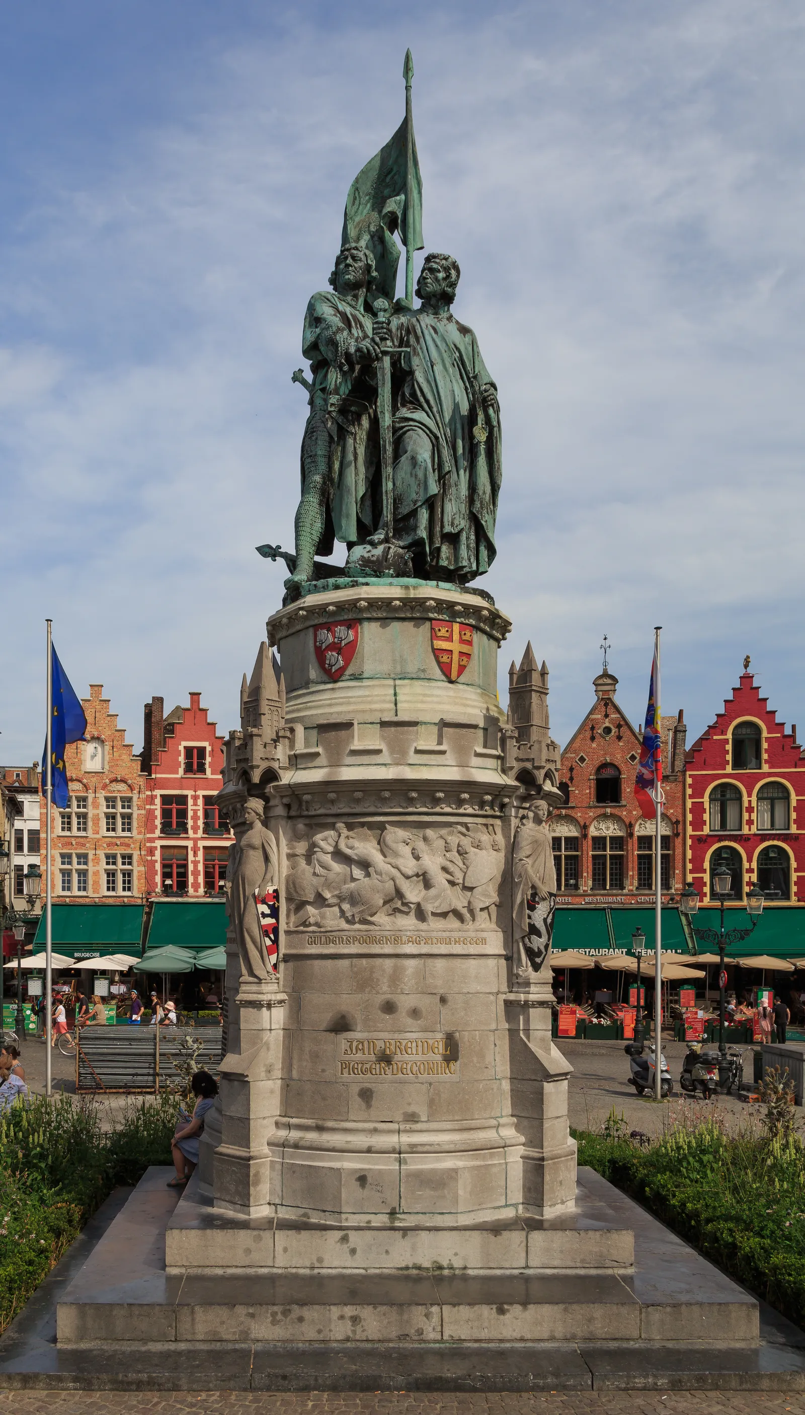 The bronze statue of Jan Breydel and Pieter de Coninck on the Markt in Bruges, two standing figures on a tall stone plinth, one holding a banner aloft
