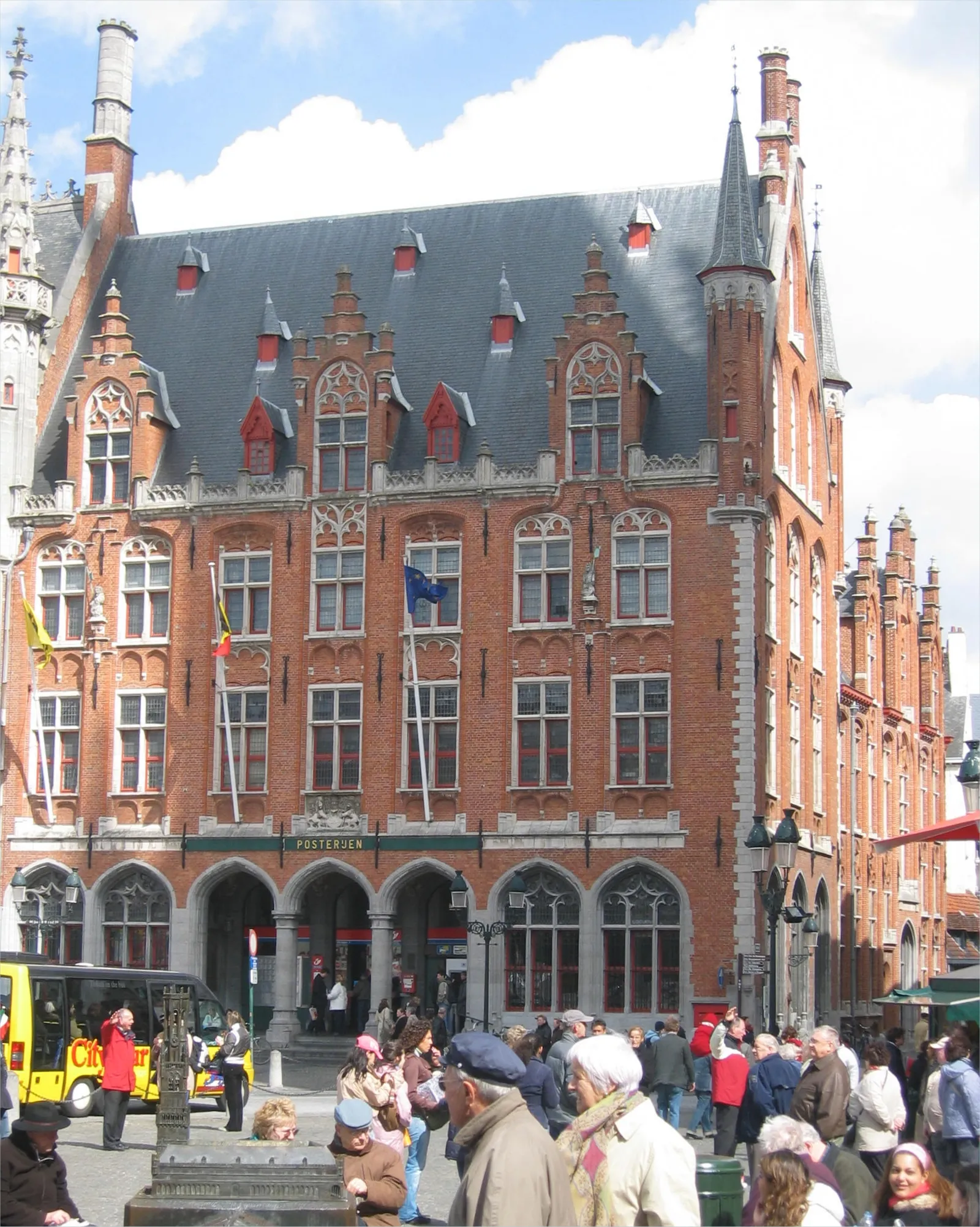 The former post office on the Markt in Bruges, a red-brick neo-Gothic block with stepped dormers, a slate roof and an arcaded ground floor lettered POSTERIJEN