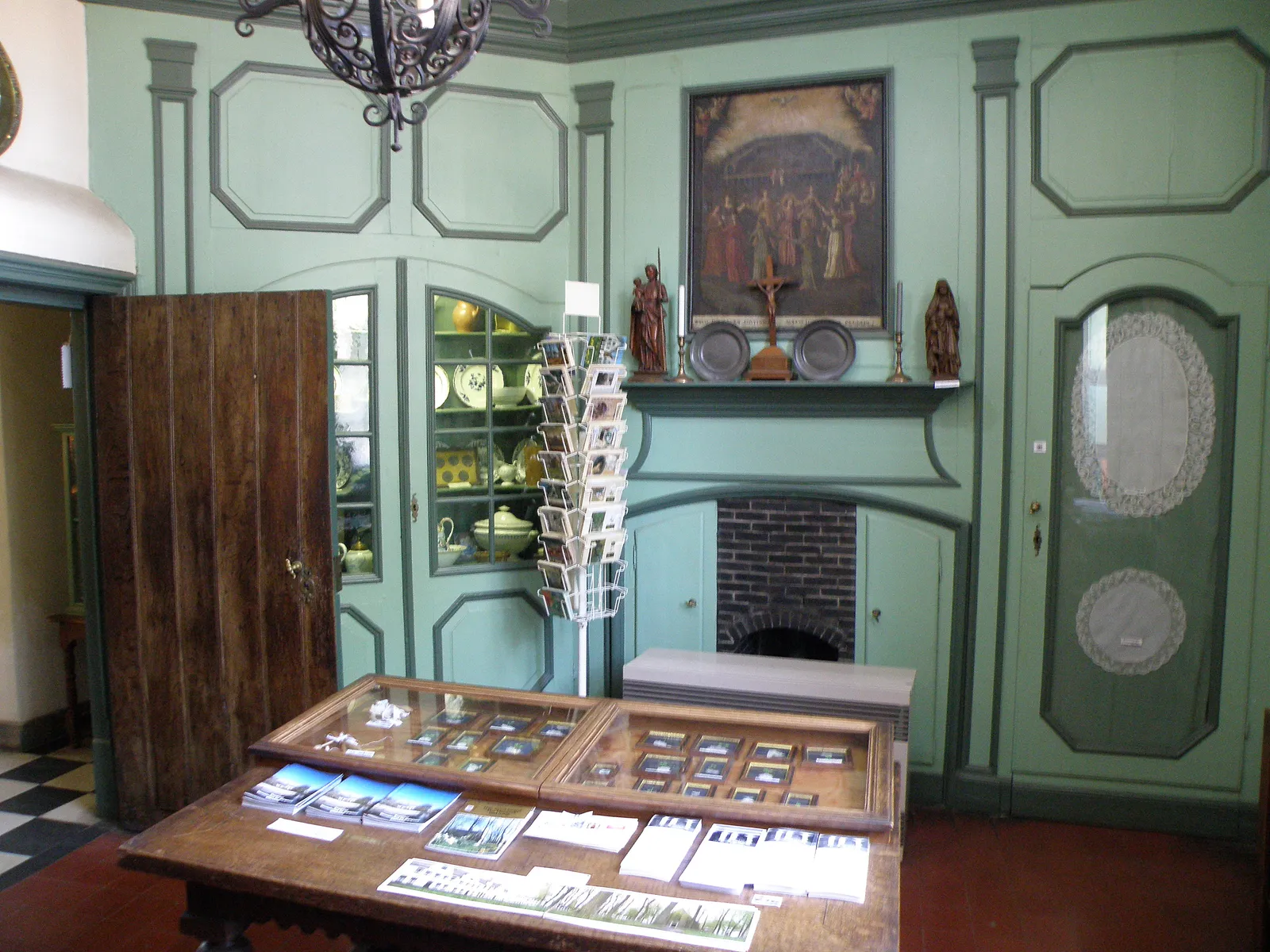 A green-panelled room inside the Beguine's House museum in Bruges, with a small brick fireplace, a glazed cabinet of crockery and a religious painting over the mantel