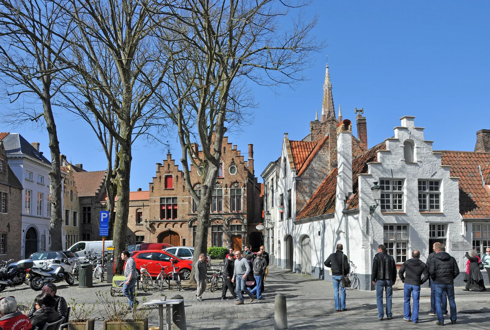 The Walplein in Bruges on a clear day, a small square of brick and whitewashed stepped-gable buildings with a church spire behind and people standing around in front of the brewery