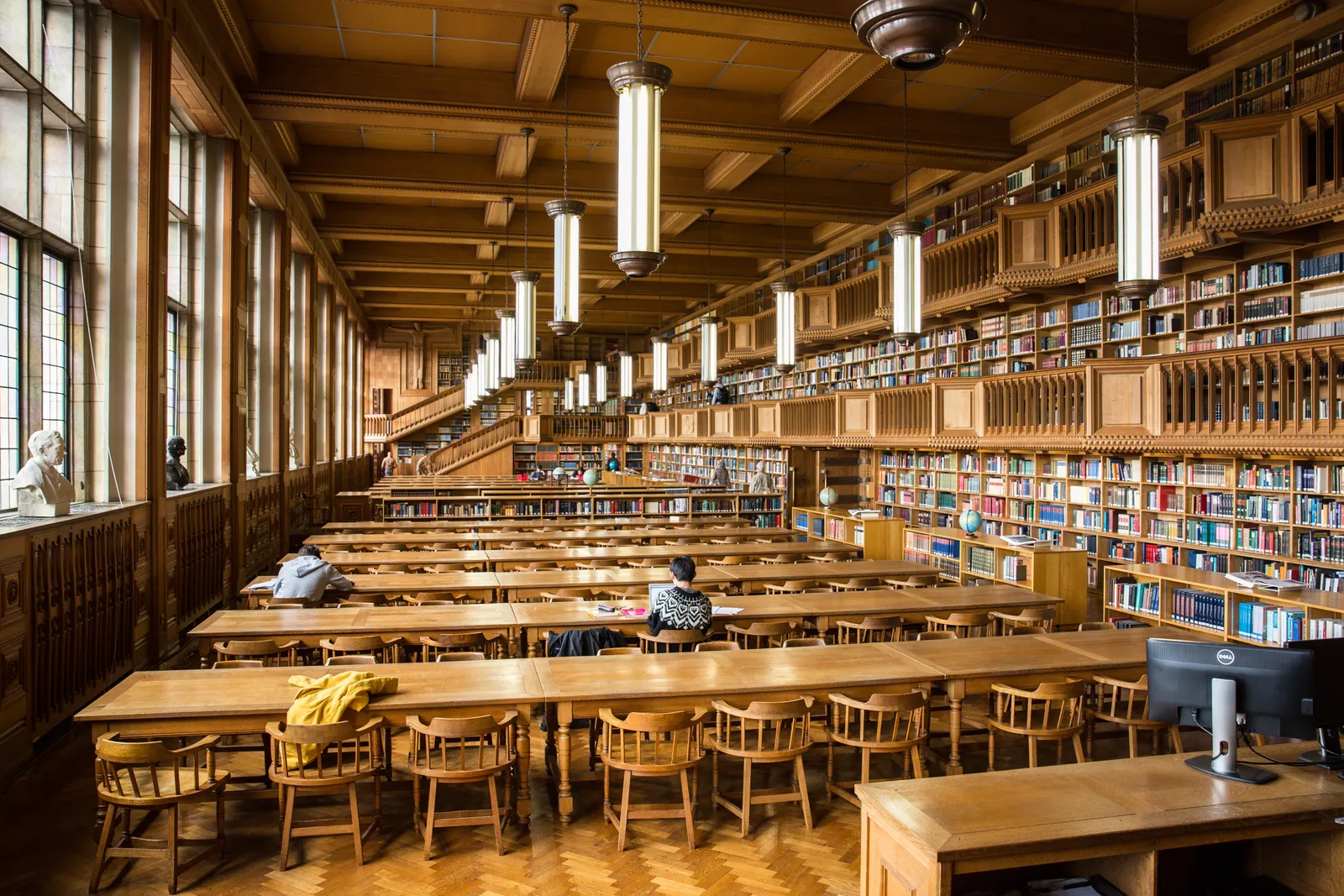 The wood-panelled reading room of the University Library in Leuven, Belgium, with long study tables, hanging lamps and two levels of bookshelves