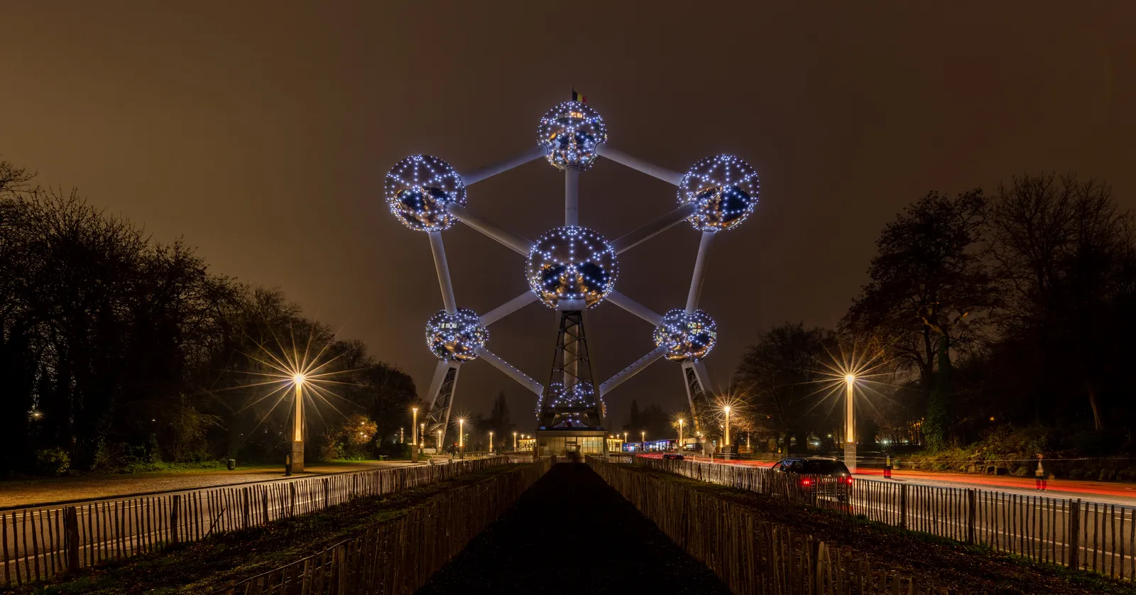 The Atomium in Brussels lit blue against a night sky, its nine linked spheres standing above a tree-lined avenue with street lamps running towards it