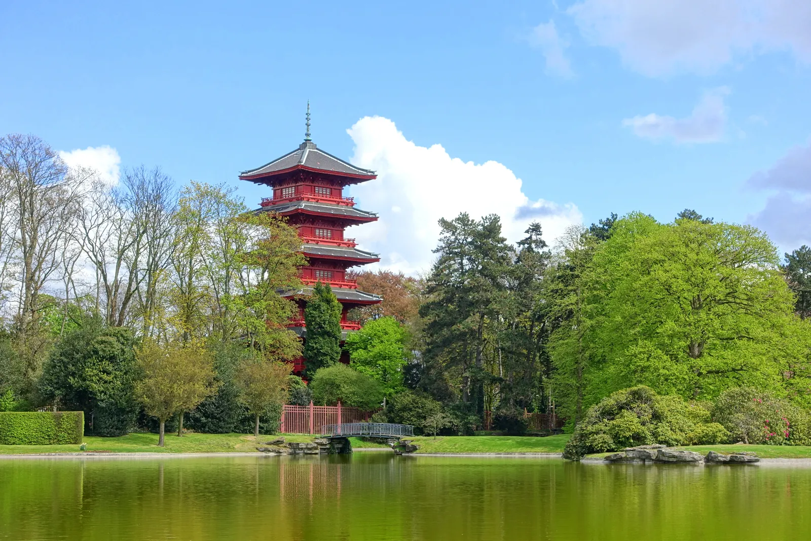 The red five-storey Japanese Tower in the royal park at Laeken, Brussels, standing among tall trees and reflected in the still green water of a pond