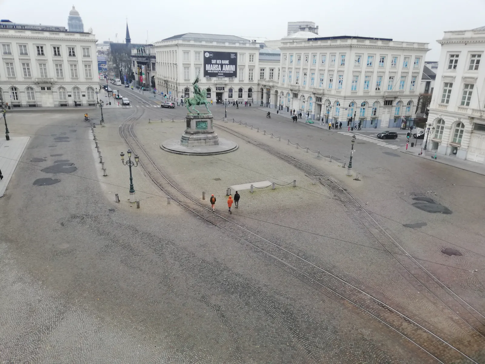 Place Royale in Brussels seen from above, a cobbled neoclassical square edged with white facades and centred on a green bronze equestrian statue, with tram rails curving across the paving