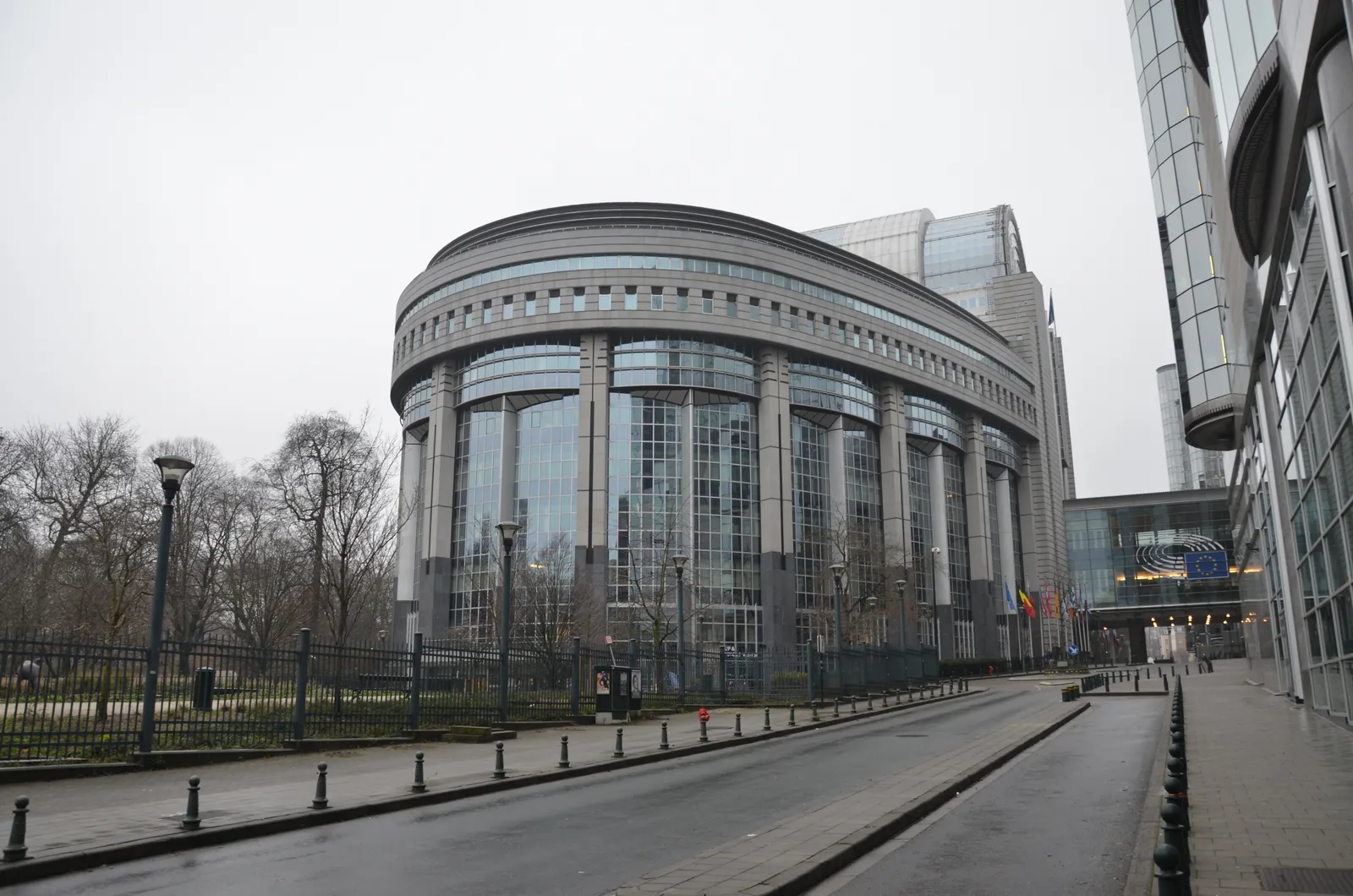 The curved glass and stone front of the European Parliament building in Brussels, its colonnaded drum rising above an empty street on an overcast day