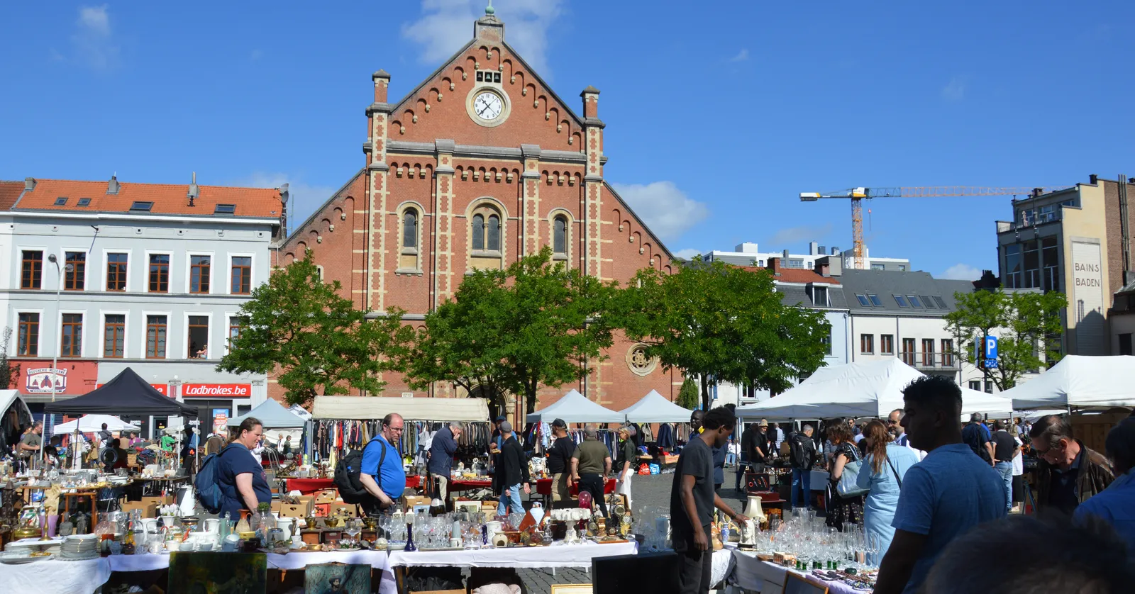 The flea market on the Place du Jeu de Balle in Brussels, goods spread over the cobbles and on trestle tables between white awnings, with the brick front of the old fire station across the square