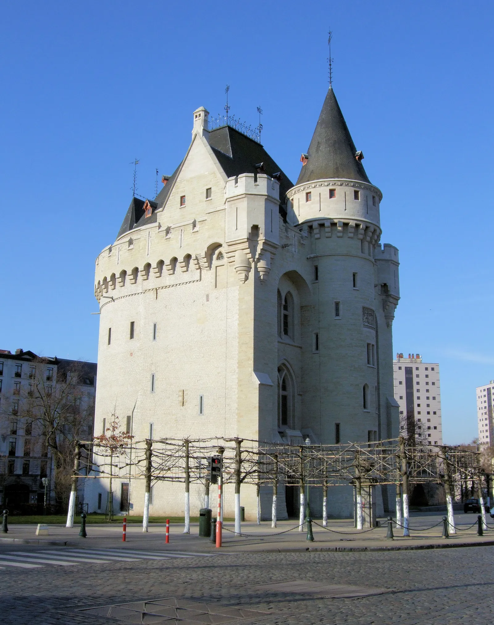 The Porte de Hal in Brussels, a white stone medieval gate tower with a conical turret and battlements, standing alone on a paved traffic island
