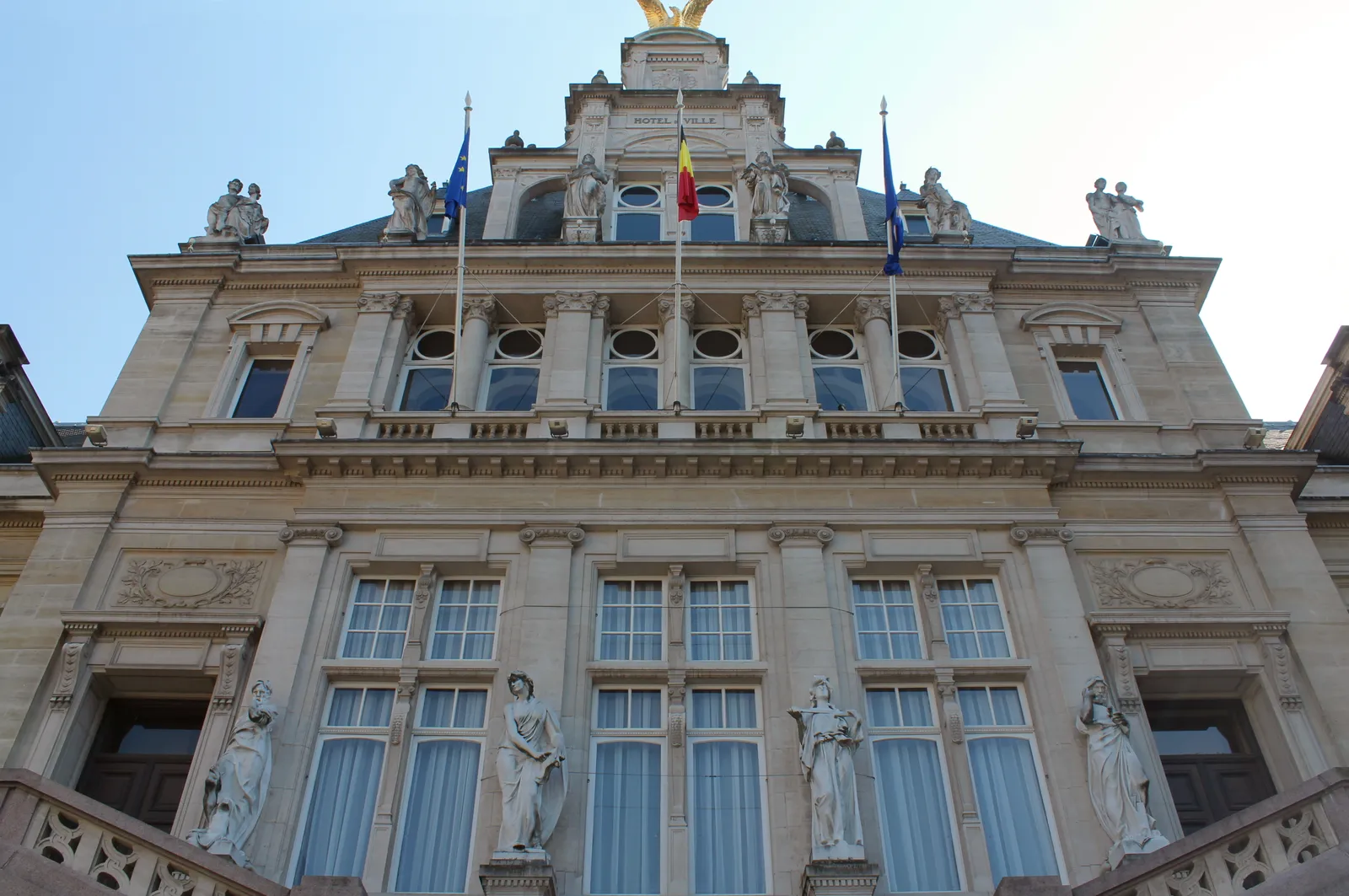 The front of the Saint-Gilles town hall in Brussels, a tall stone and brick facade in neo-Flemish Renaissance style with carved figures between the windows and flags above the entrance