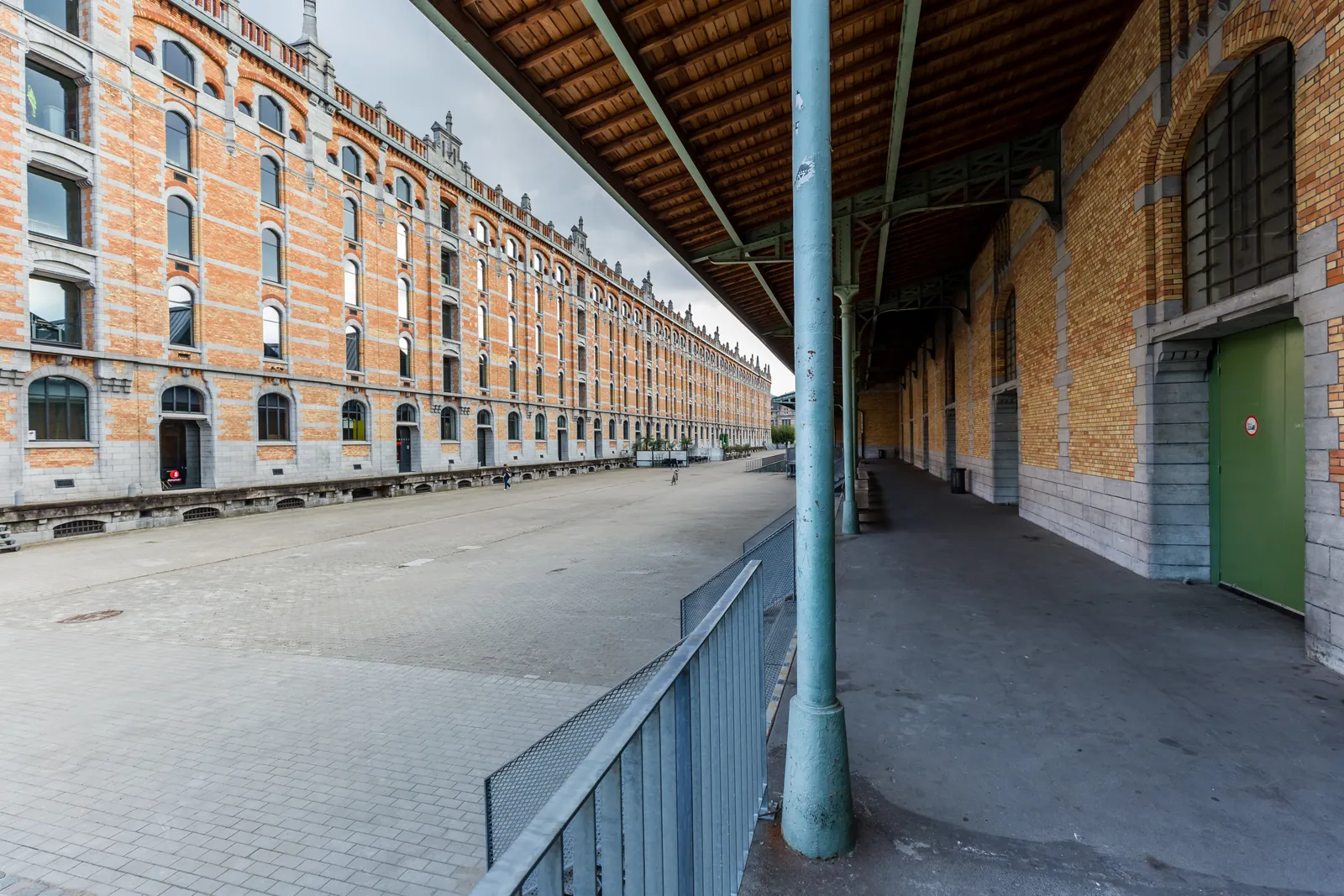The long brick front of the Entrepôt Royal warehouse at Tour & Taxis in Brussels, its repeated arched windows running the length of an empty cobbled yard