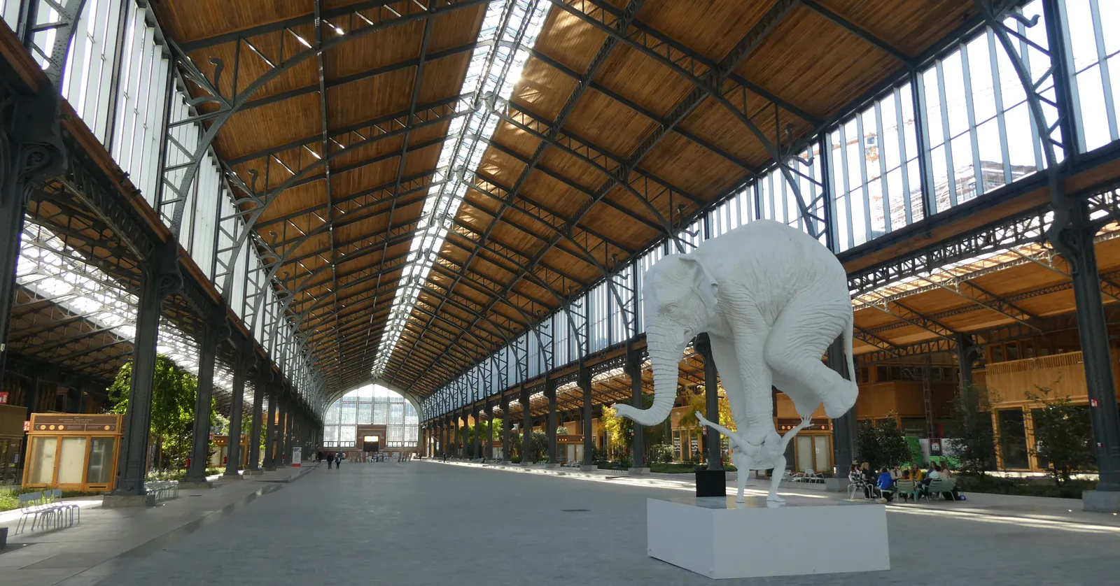The interior of the Gare Maritime in Brussels, a vast restored freight hall of iron trusses and glazed roof panels running the length of the building over a paved public floor