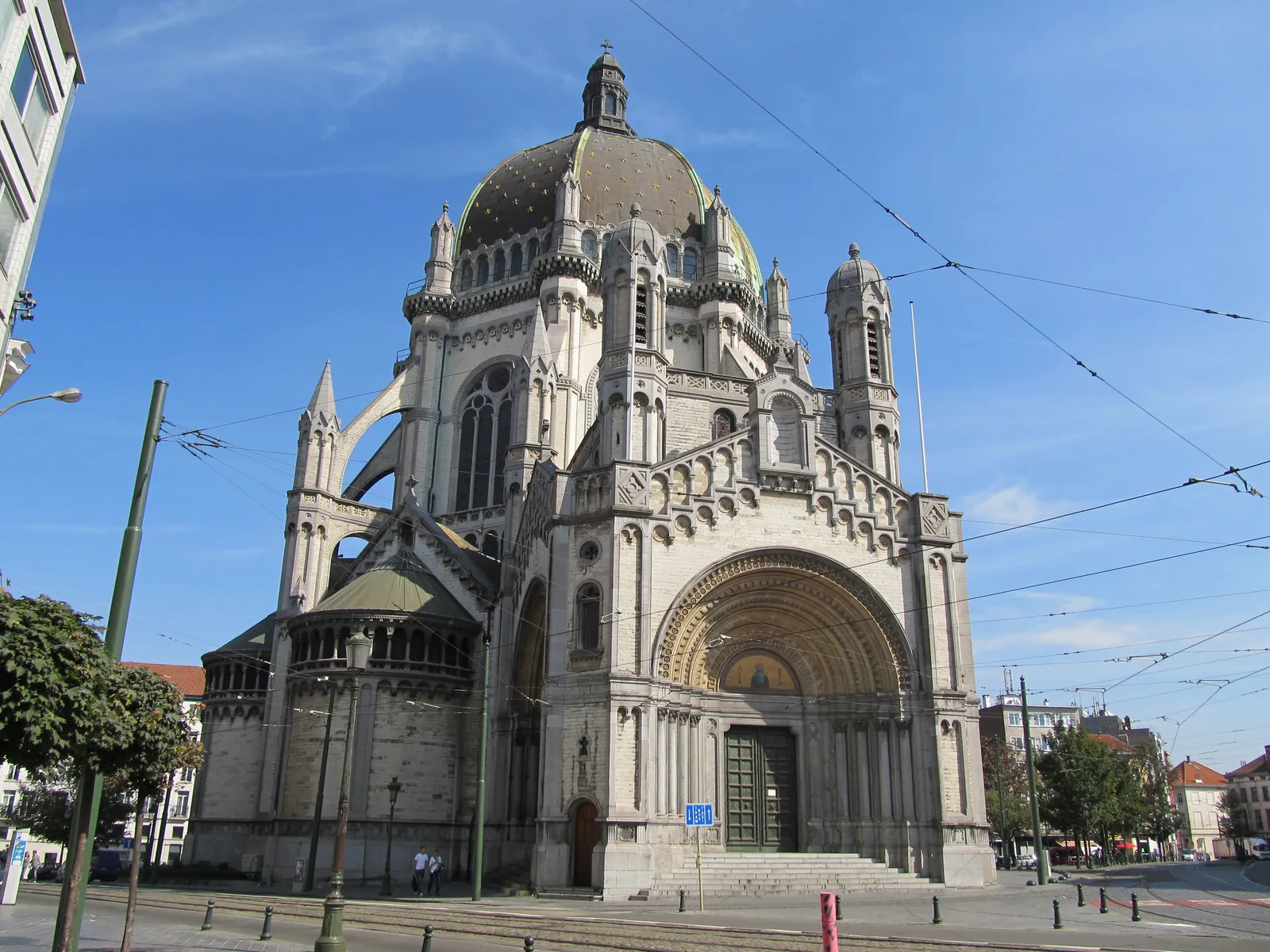 Saint Mary's Royal Church in Schaerbeek, Brussels, an octagonal stone church with a green and gold dome and a deep round-arched porch, standing at the end of a tram-tracked street