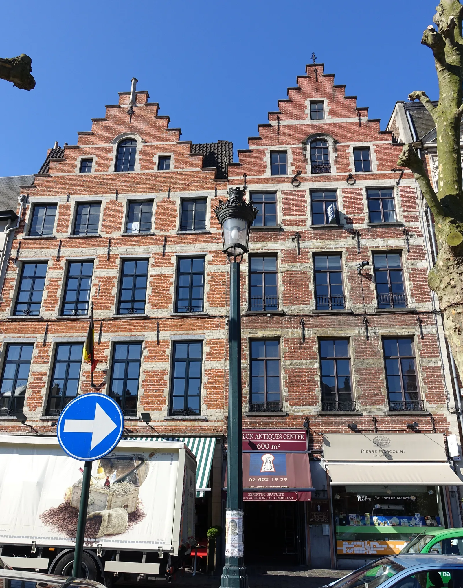 Stepped-gable brick houses on the Place du Grand Sablon in Brussels, with an antiques centre and a chocolatier's shopfront at street level under a bright blue sky