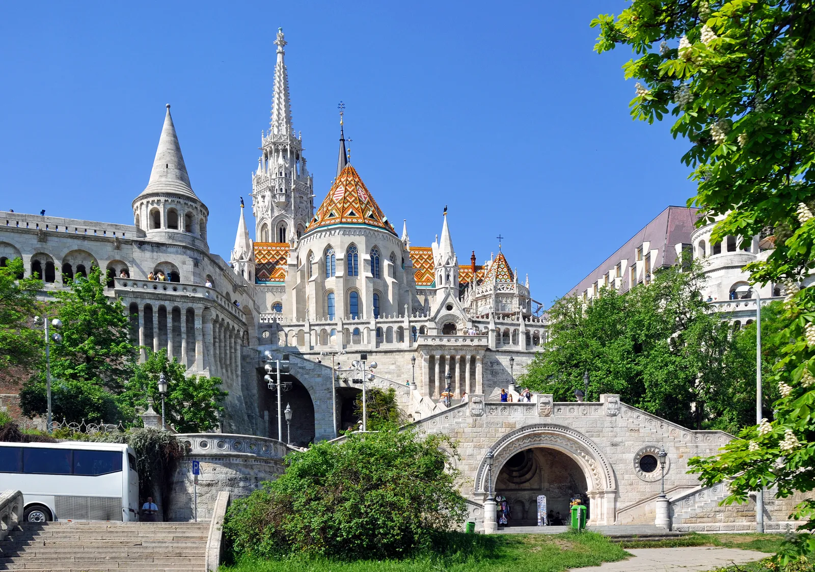 Fisherman's Bastion in Budapest, white stone arcades and conical-roofed turrets with steps climbing between them, and the tiled roof and spire of Matthias Church rising behind