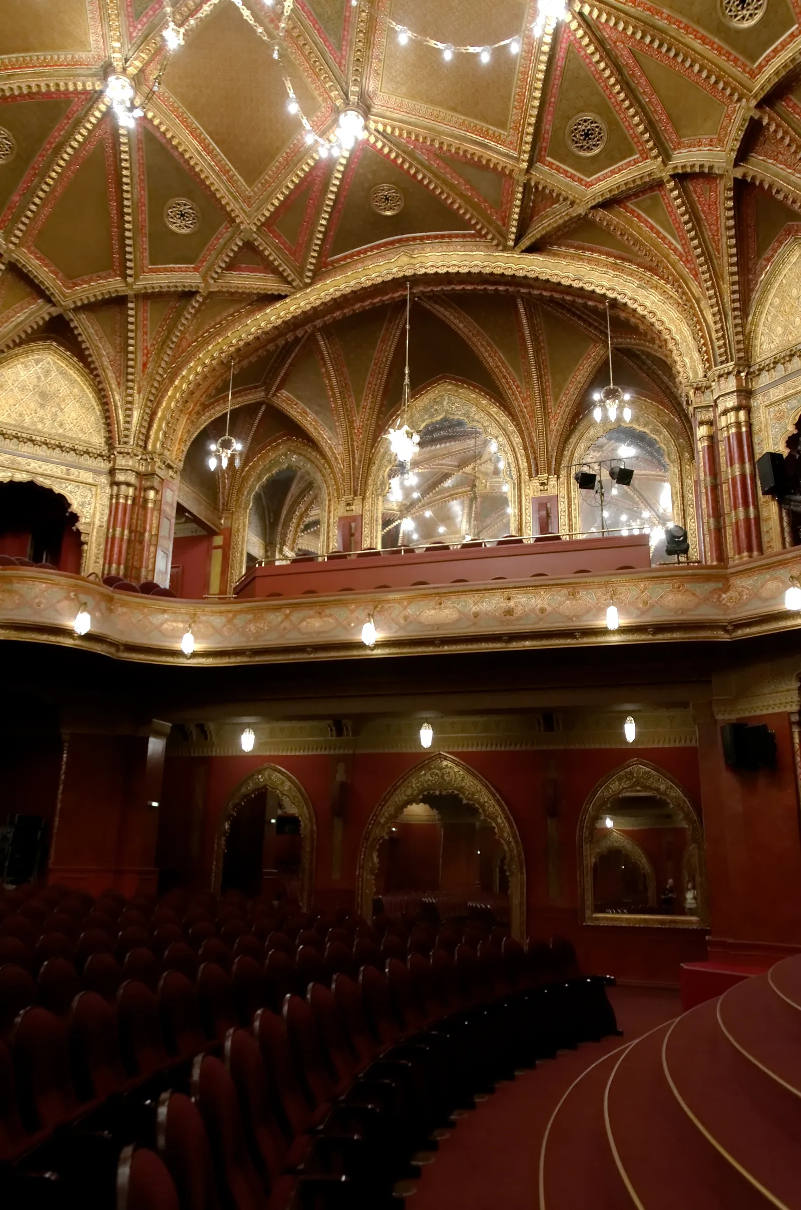 The auditorium of the Uránia cinema in Budapest, rows of red seats below a gilded vaulted ceiling and a balcony carried on horseshoe arches picked out in gold and red