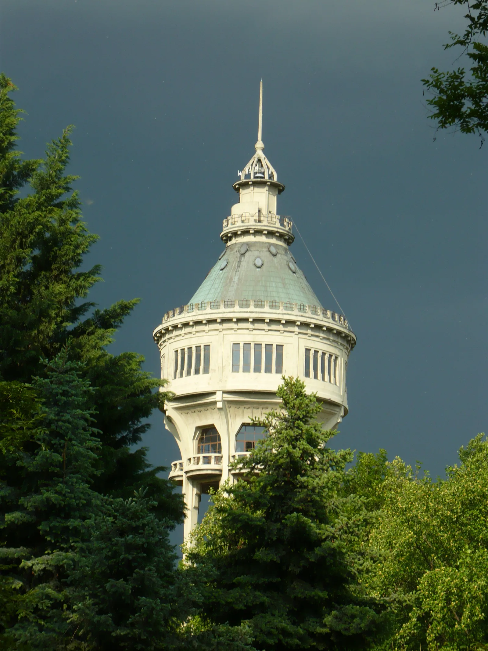 The water tower on Margaret Island in Budapest, an octagonal white tower on open legs with a colonnaded gallery and a green copper dome, rising above the treetops against a dark sky