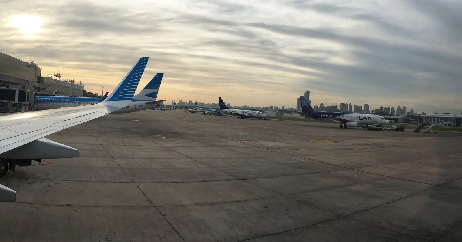 The apron at Aeroparque Jorge Newbery in Buenos Aires at dawn, with parked airliners across the concrete and the towers of the city skyline standing directly behind the airfield