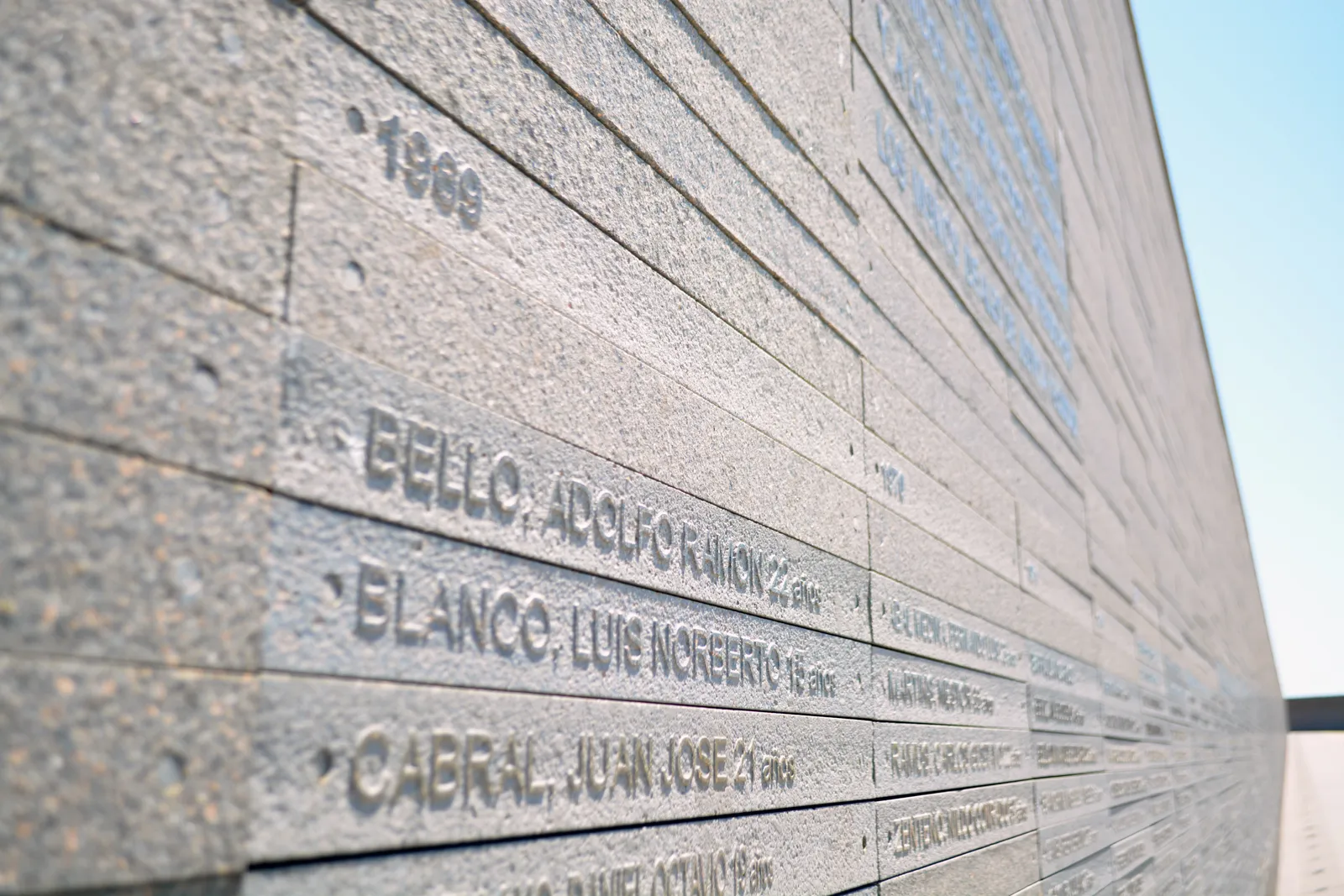 A close view along the stone wall at the Parque de la Memoria in Buenos Aires, its slabs cut with the surnames, first names and ages of the disappeared beneath the year 1969