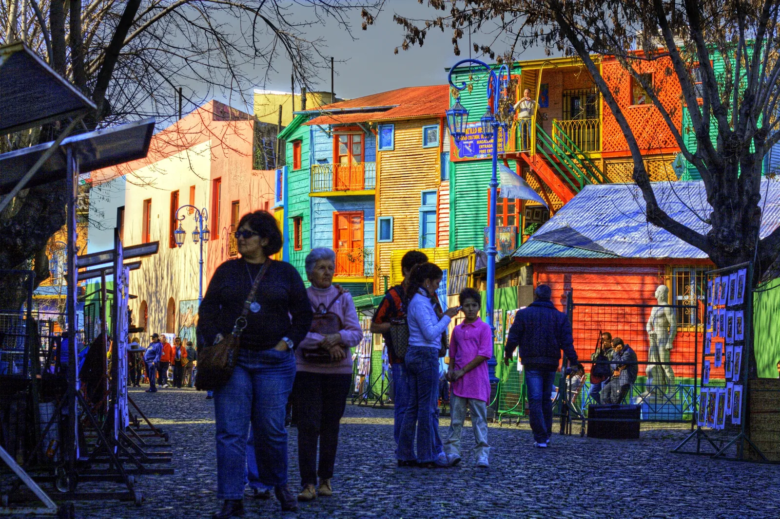 The Caminito passage in La Boca, Buenos Aires, lined with corrugated-iron houses painted in blocks of green, blue, orange and yellow, with visitors walking between craft stalls along the cobbles