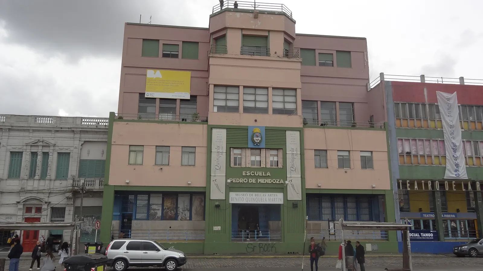 The four-storey front of the Escuela Pedro de Mendoza on the La Boca waterfront in Buenos Aires, painted green and pink with the school's name and crest across the entrance