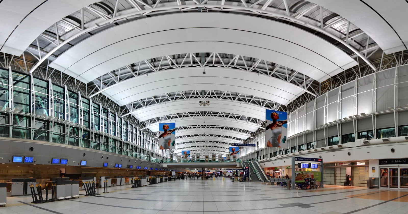 The wide barrel-vaulted concourse at Buenos Aires Ezeiza airport, with a curved white steel roof running the length of the hall over check-in desks and an almost empty floor