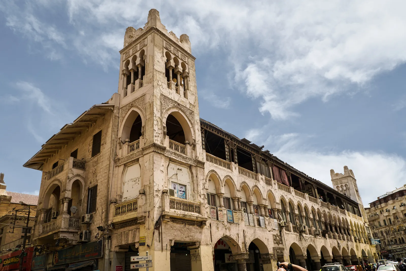 A corner building at Korba in Heliopolis, its ground floor a run of horseshoe arches over the pavement and a square tower with arched windows above, seen from street level