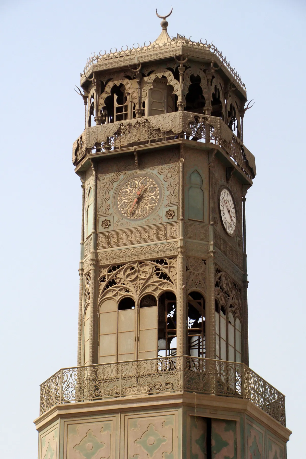 The ornate copper clock tower in the courtyard of the mosque of Muhammad Ali, an octagonal pavilion of pierced metalwork with a patterned clock face on one side and a Roman-numeral dial on the next