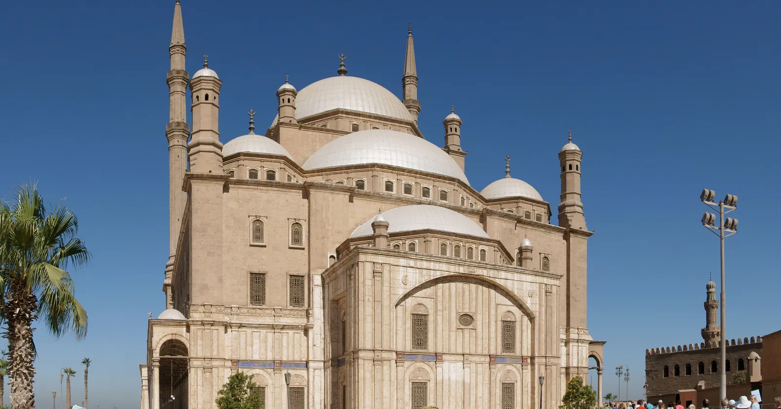 The mosque of Muhammad Ali at the Cairo Citadel seen from outside, its central dome ringed by smaller half-domes with two slim pencil minarets rising either side against a clear blue sky