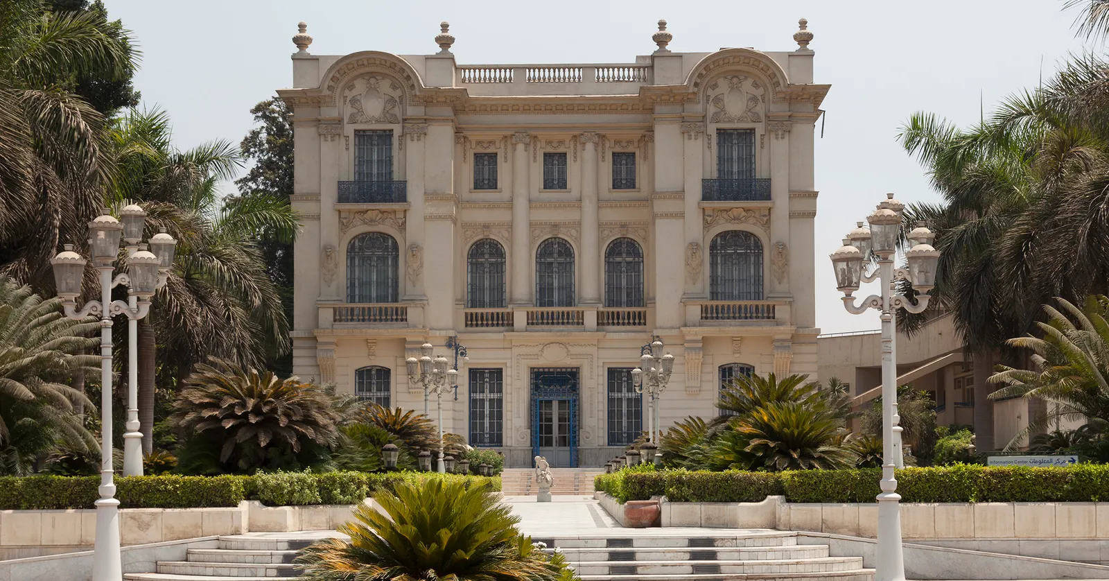 The Mahmoud Khalil Museum in Giza, a pale three-storey mansion with tall arched windows and a stone balustrade along the roof, palms and lamp standards lining the drive in front of it