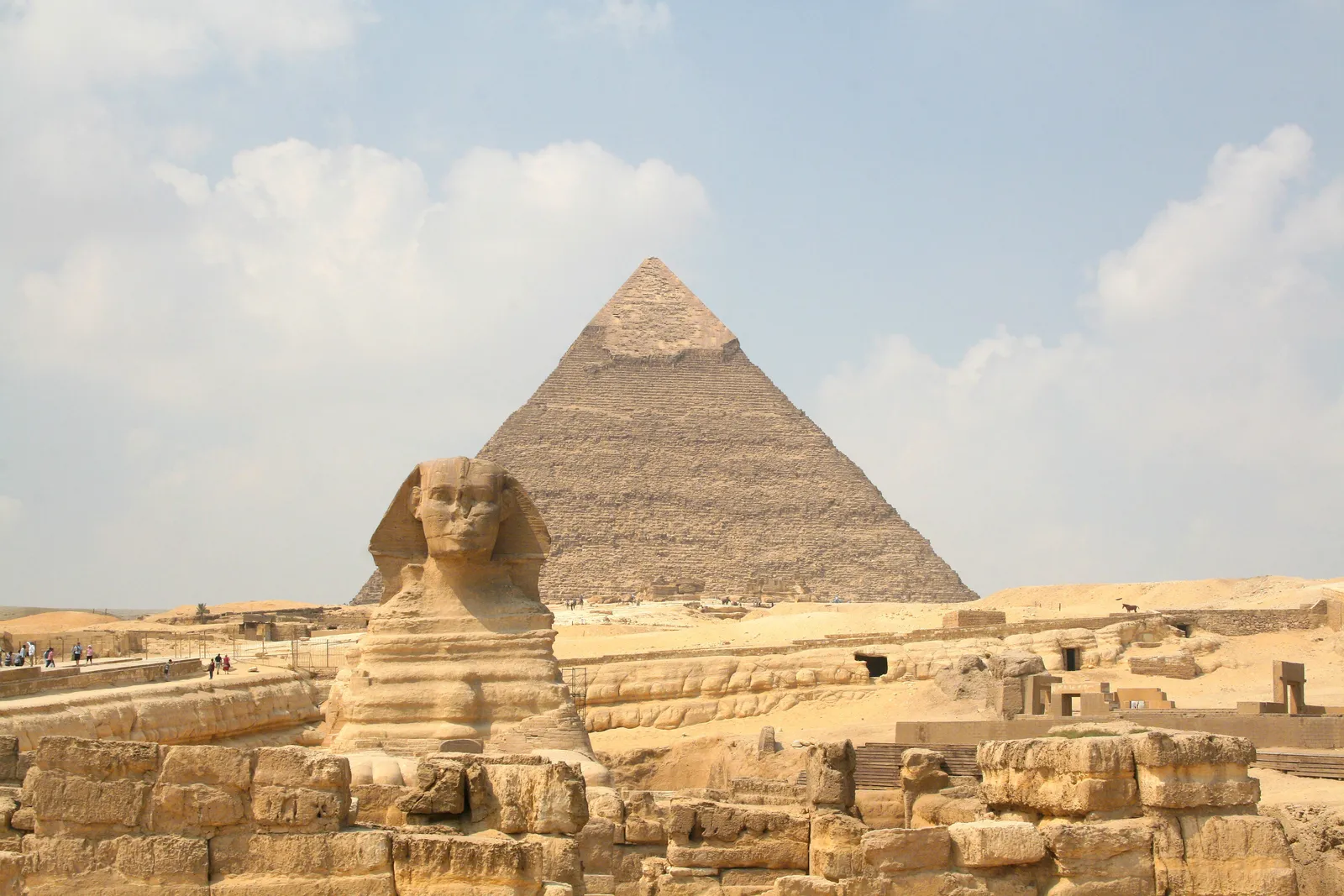 The Great Sphinx of Giza seen head-on from the east, sitting below the level of the surrounding stone, with the pyramid of Khafre rising directly behind it